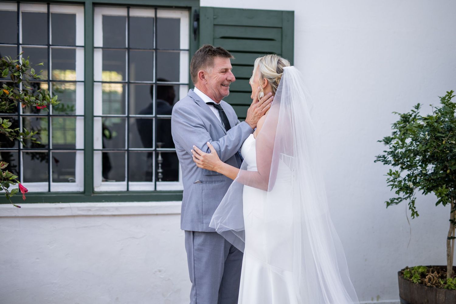 A couple shares their first look moment in an outdoor courtyard setting with white walls and greenery.
