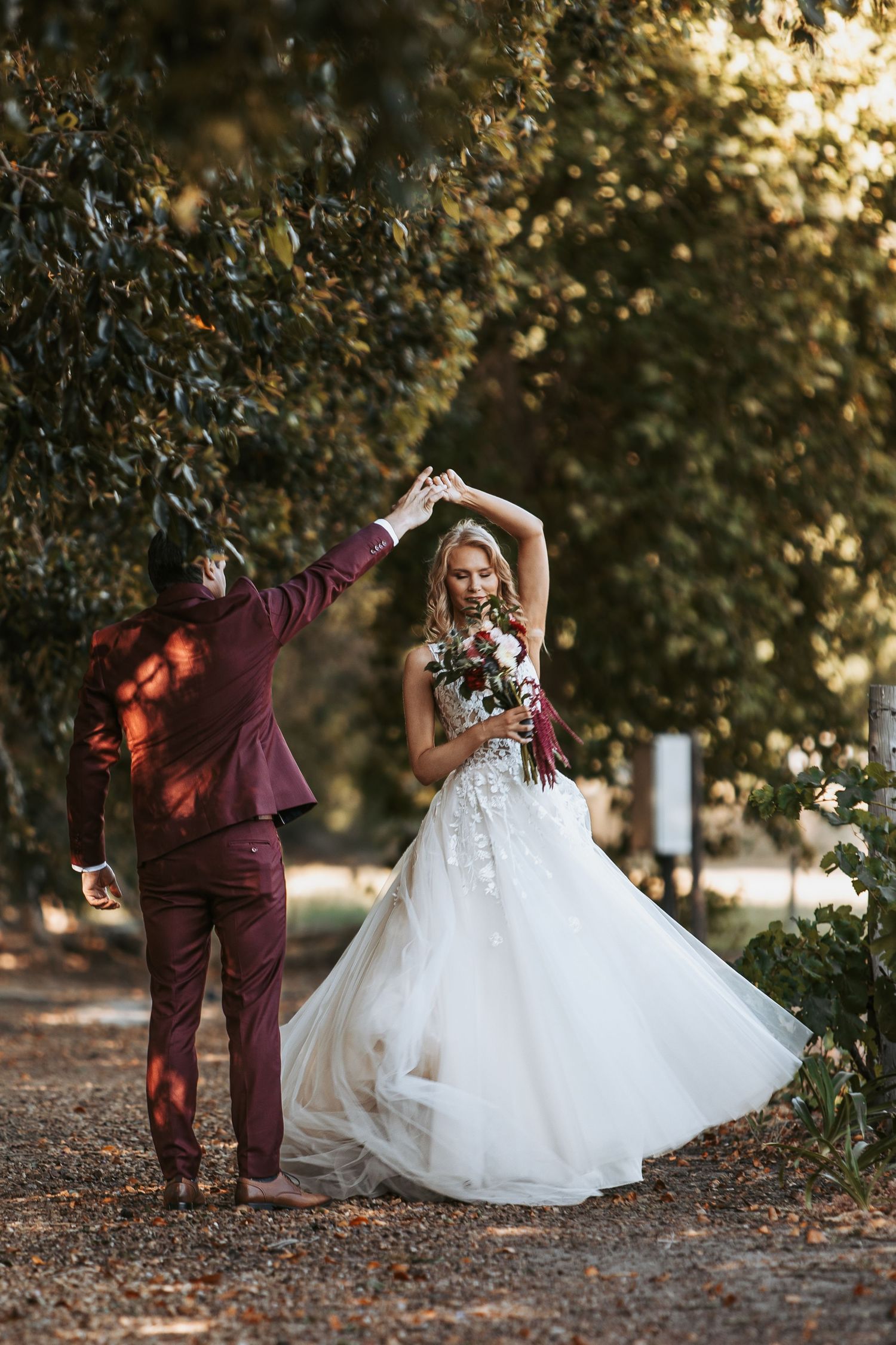 Wedding couple in burgundy suit and white dress dancing together on fallen autumn leaves.