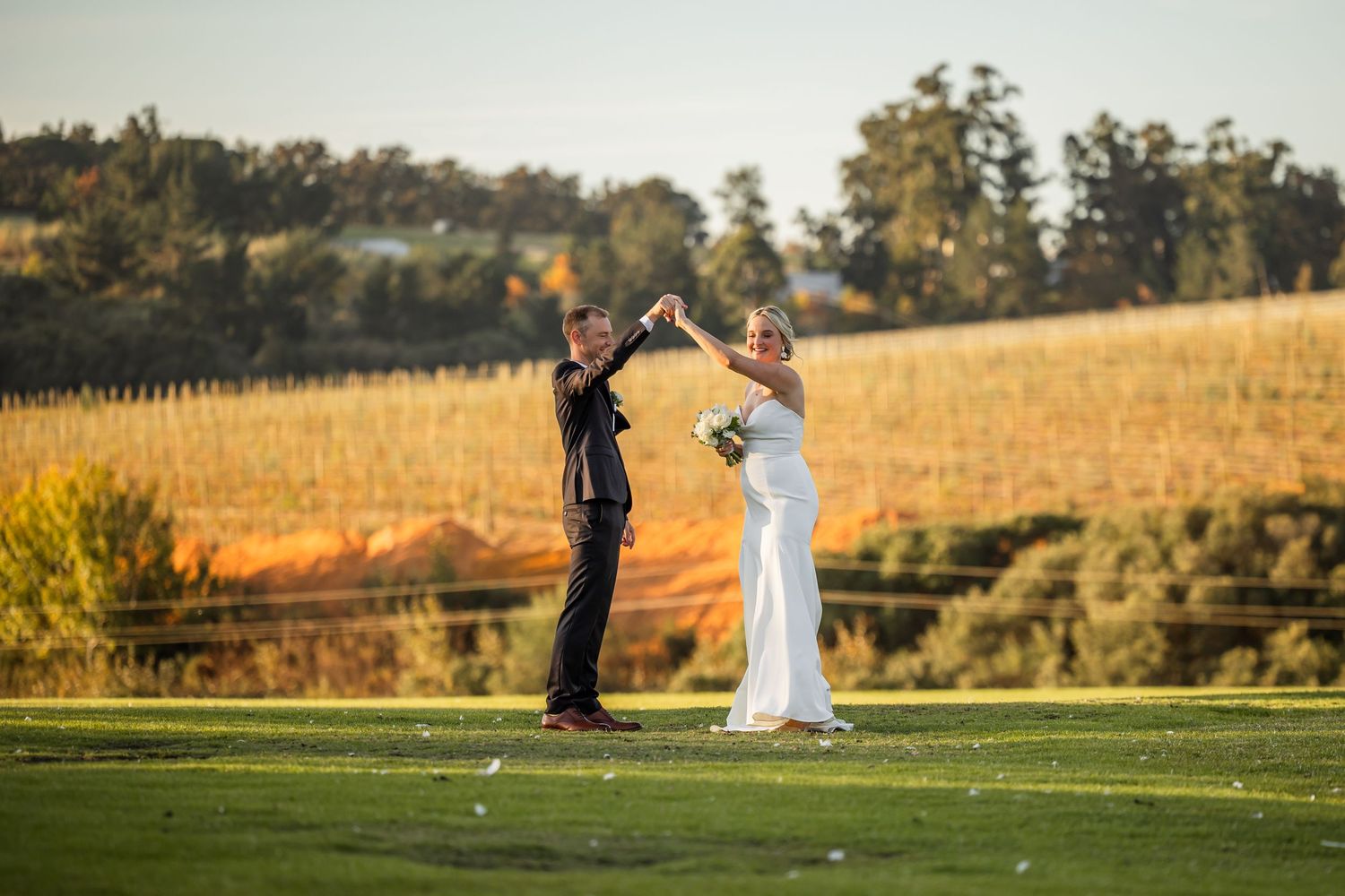 Panoramic wedding portrait of a couple in a golden sunset field with rolling hills in the background.