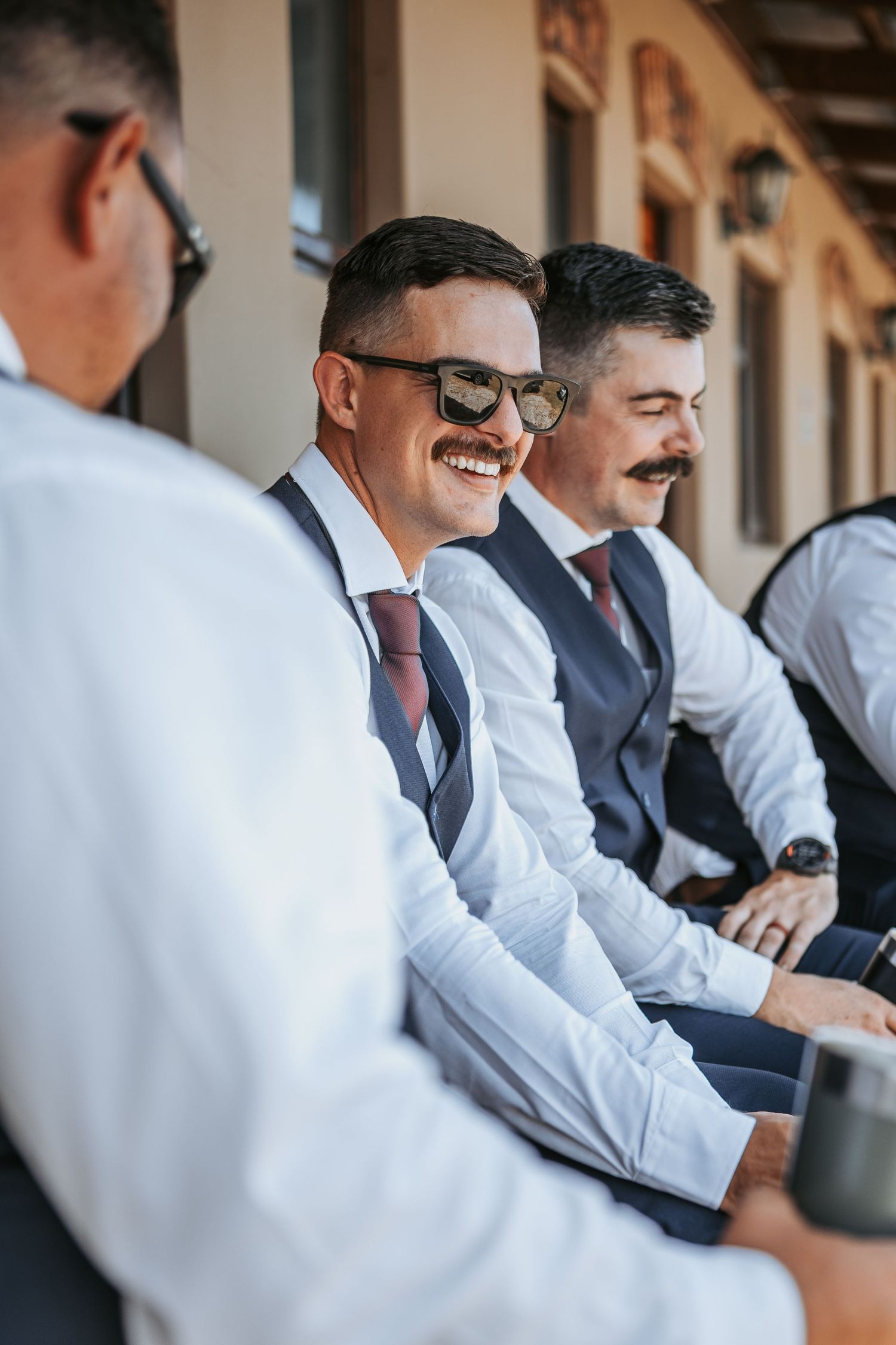 Wedding party members laughing together on a sunny patio.