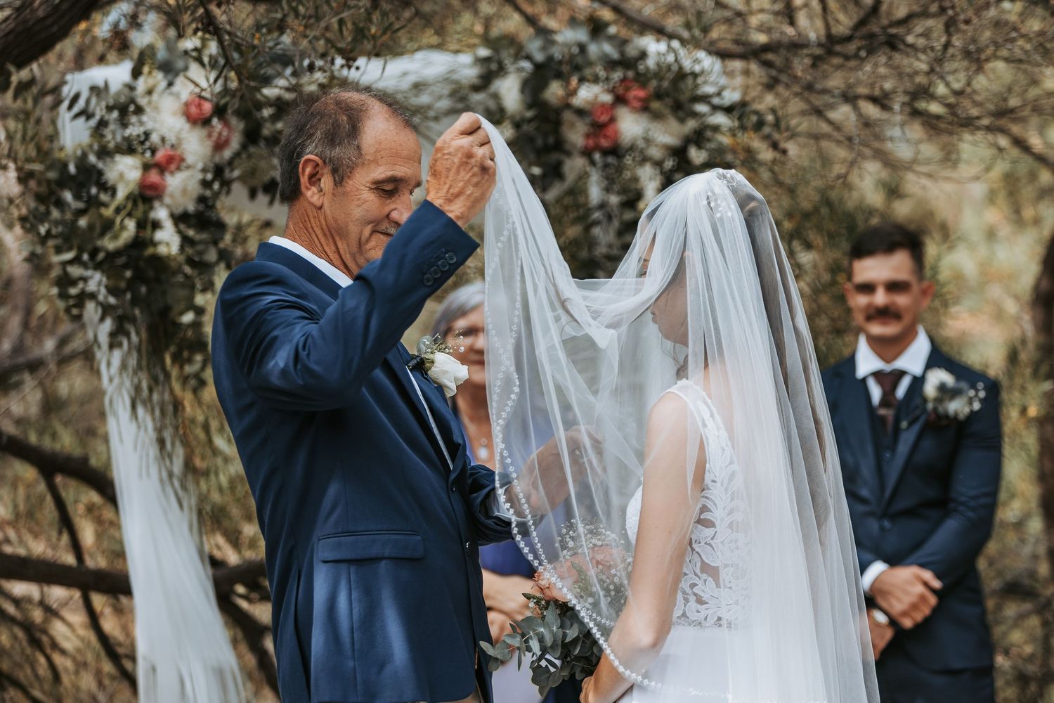 Wedding ceremony taking place outdoors with guests gathered under blooming trees.