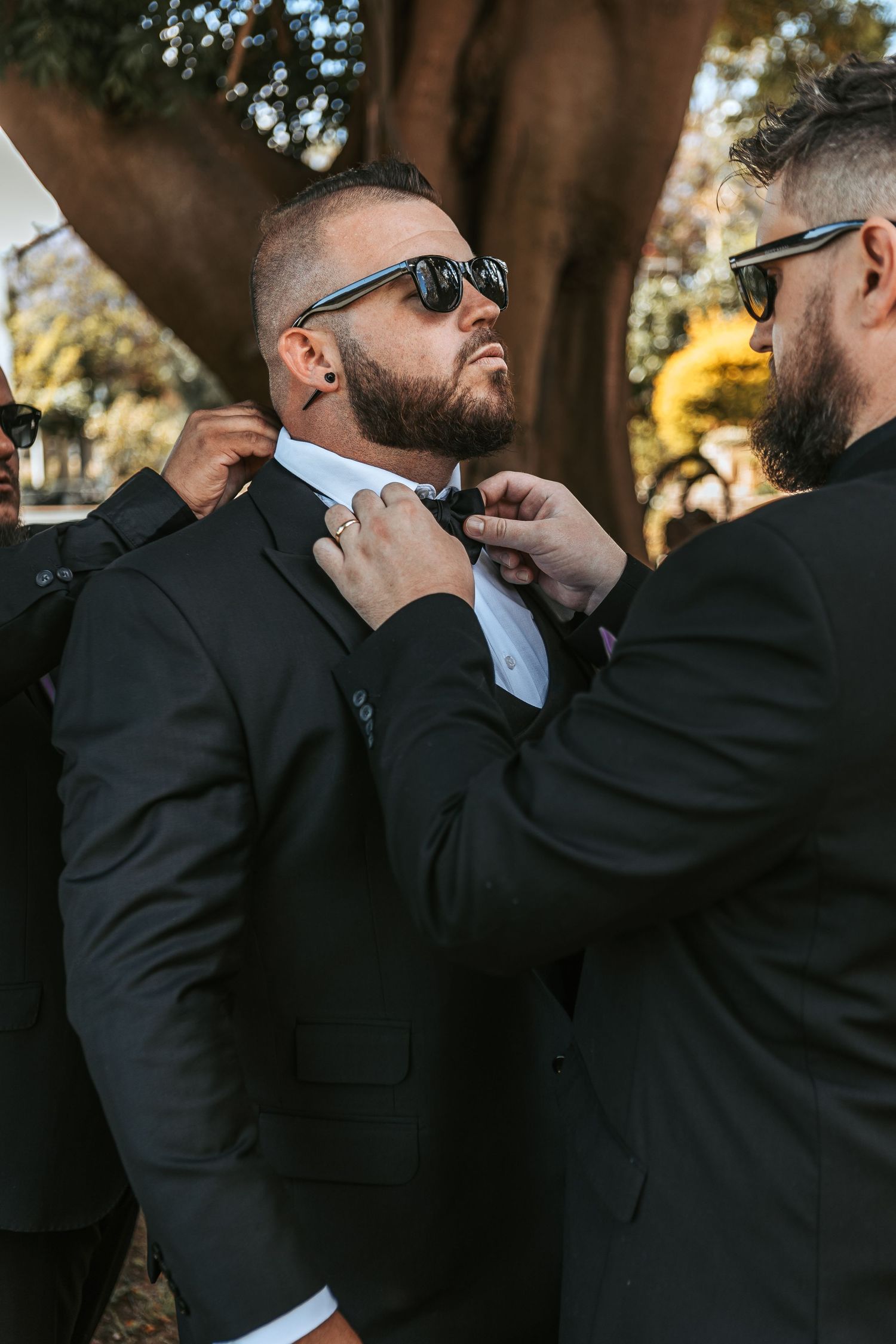 Groomsmen in black suits adjusting their collars and ties before the ceremony.