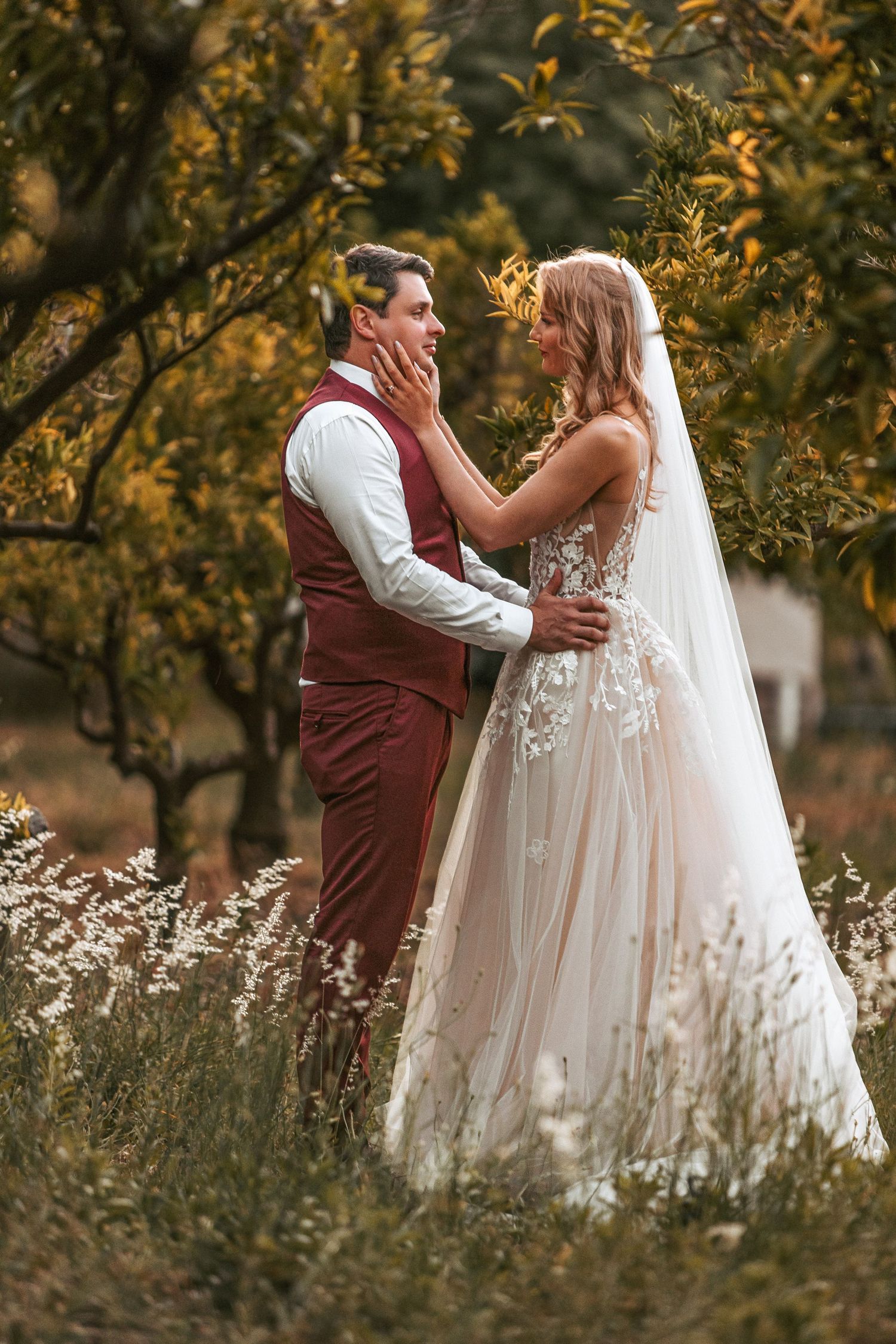 A tender wedding moment photographed among fall foliage and tall grasses at sunset.