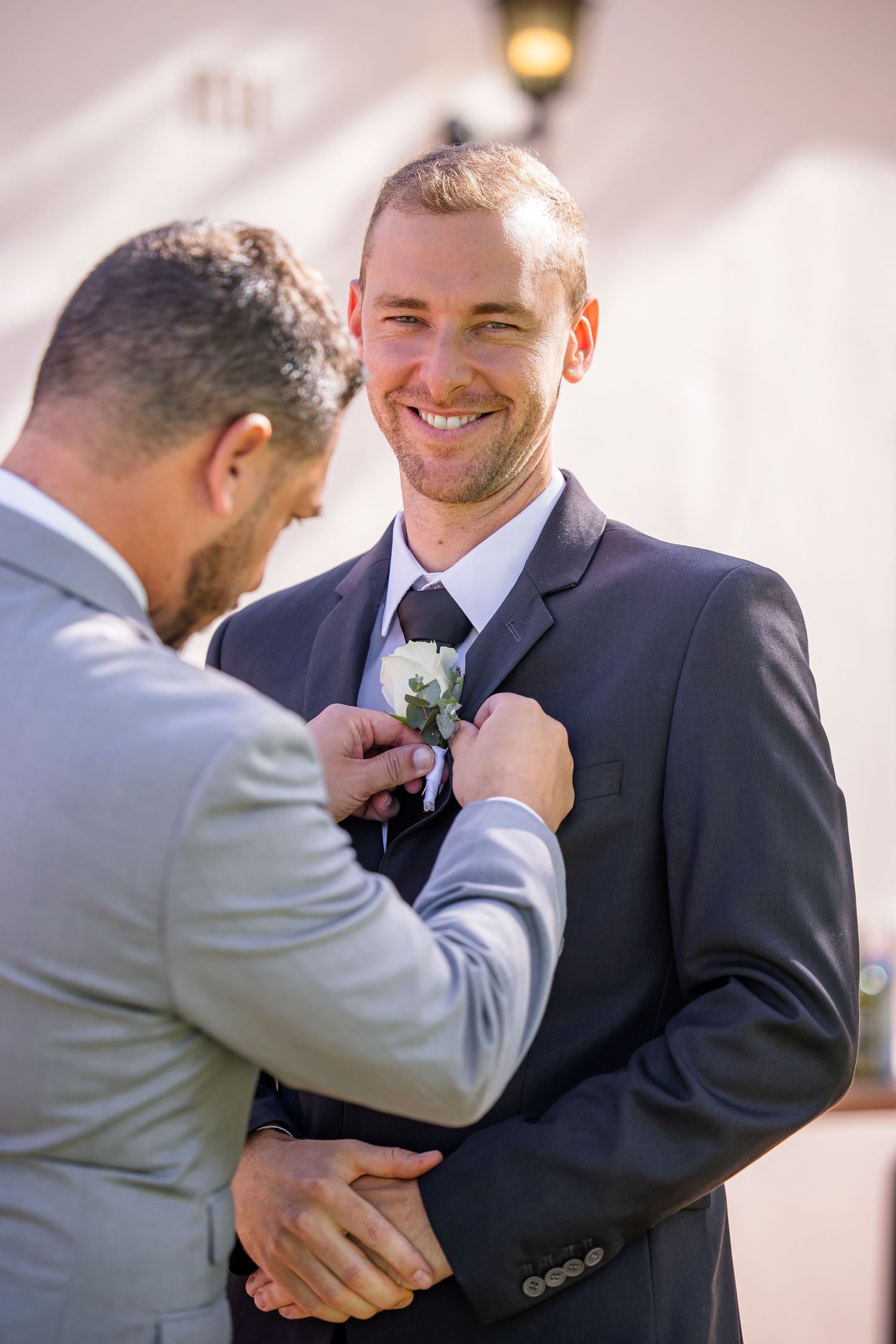 Groomsmen in navy and grey suits share emotional embraces during pre-wedding preparations.
