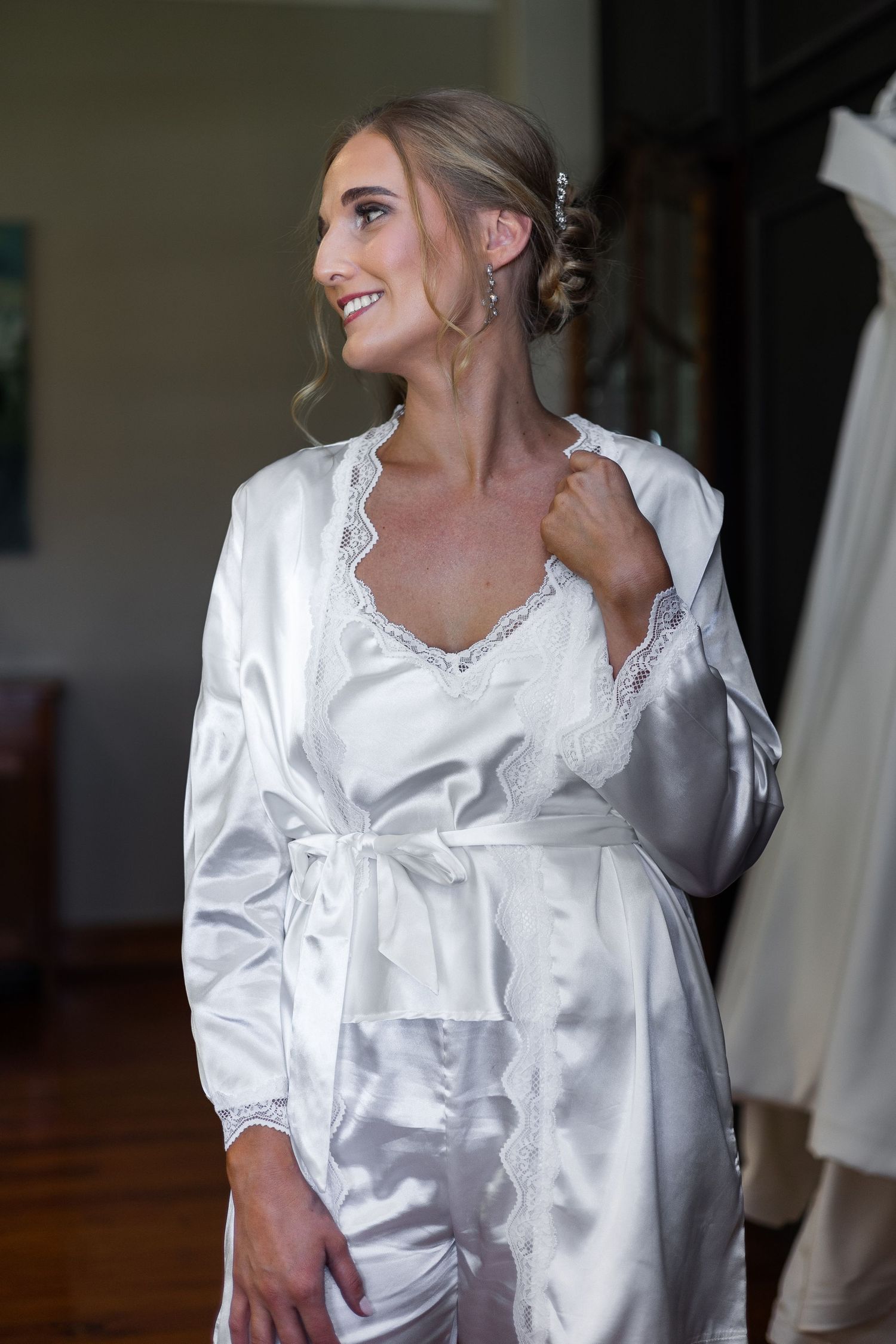 Elegant bride in white satin robe smiles while getting ready for her wedding ceremony.