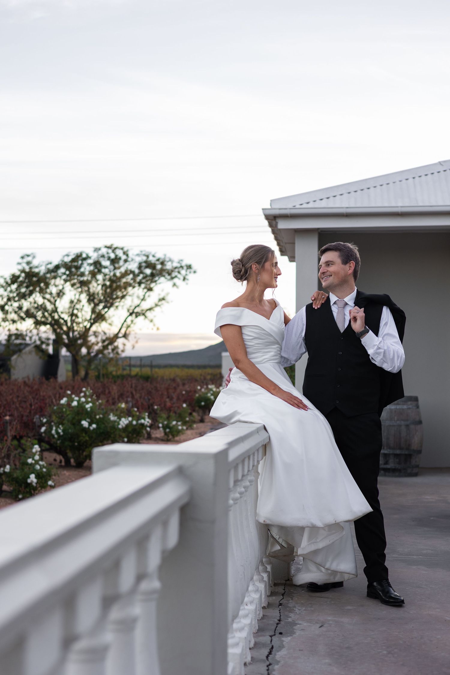 Bride and groom smiling at each other on a white balcony terrace at sunset.
