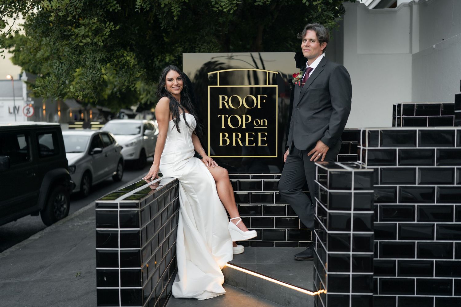 Bride and groom posing at Rooftop on Bree venue entrance, bride in white gown, groom in dark suit.