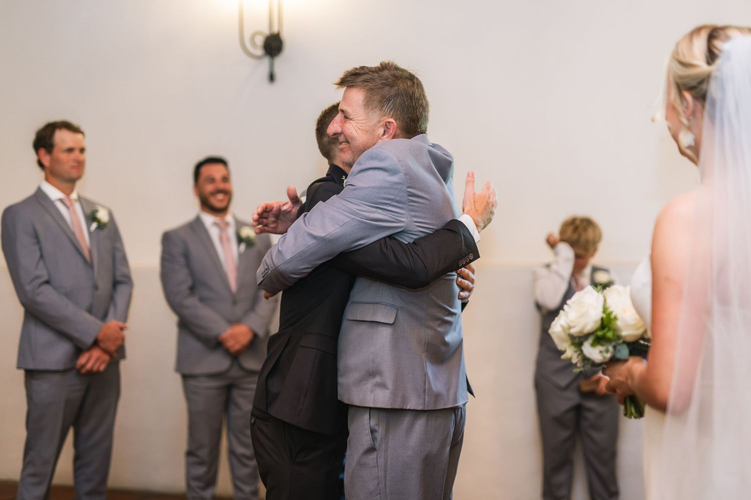 Wedding guests embrace and celebrate during an emotional indoor reception moment.