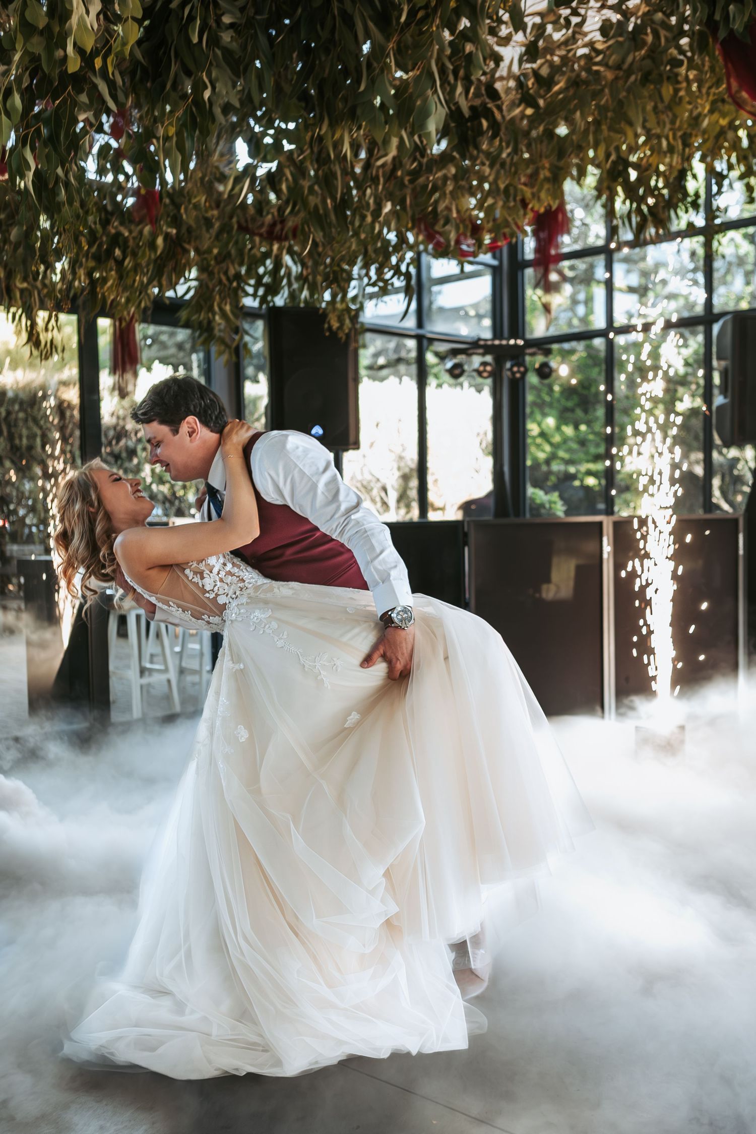 A couple performs a dramatic dip during their wedding dance surrounded by fog and sparklers.