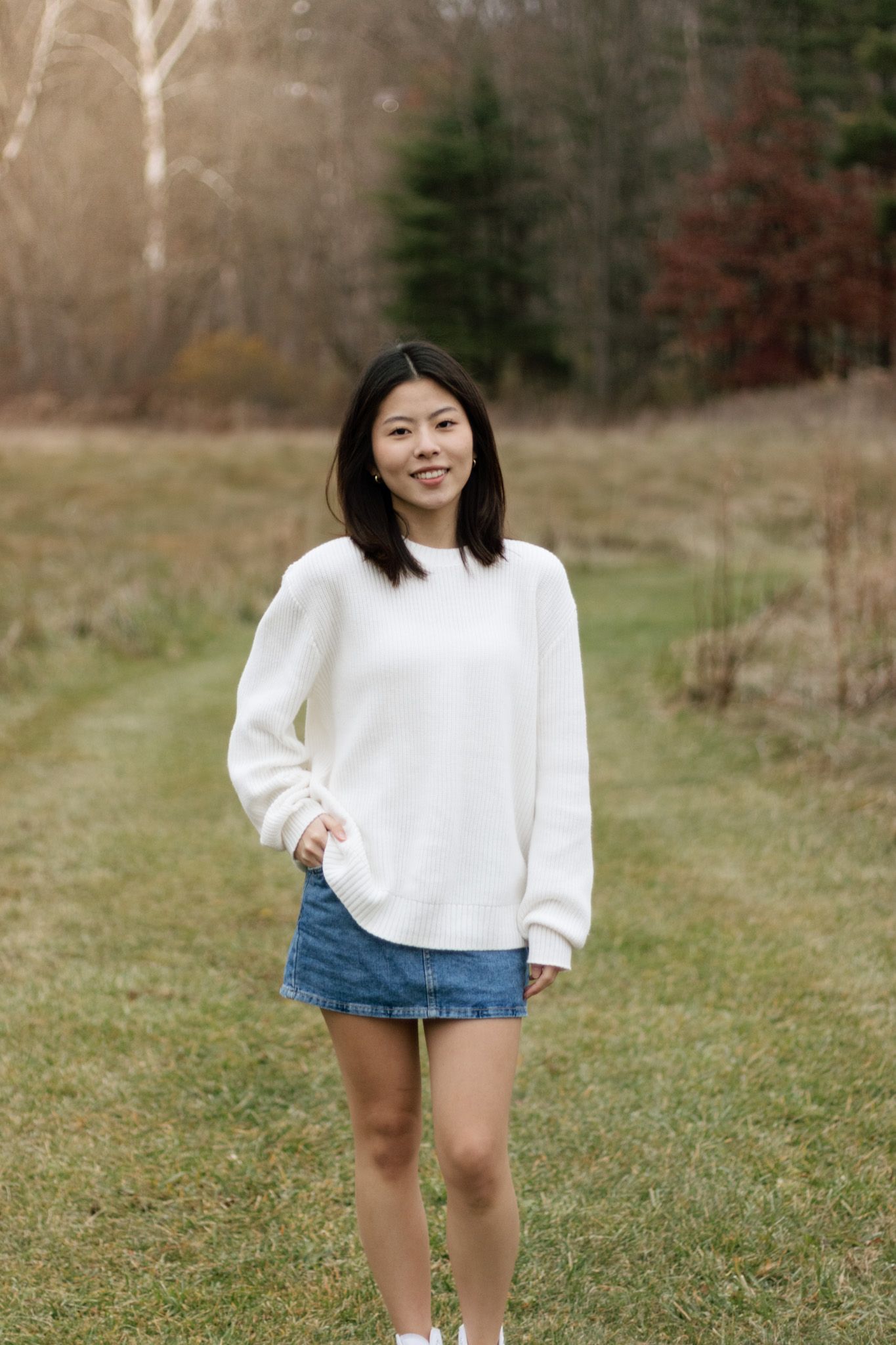 Casual outdoor portraits in white sweater and denim shorts against natural backdrop.