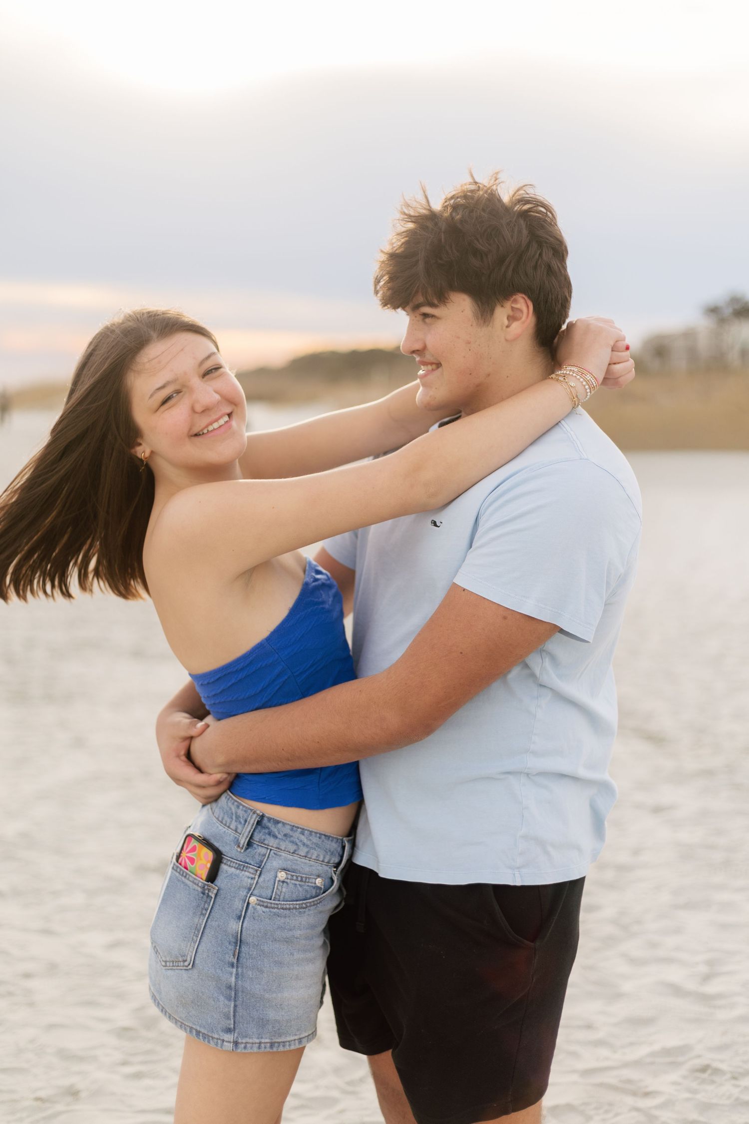 A couple shares a playful embrace while dancing together on a sandy beach at sunset.