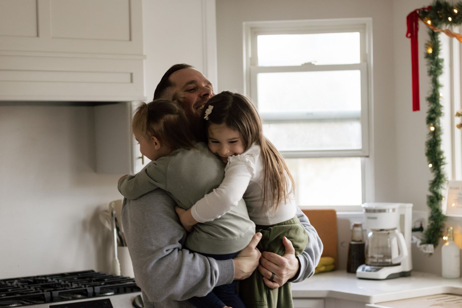 Family sharing a warm group hug in their bright kitchen with holiday decorations.