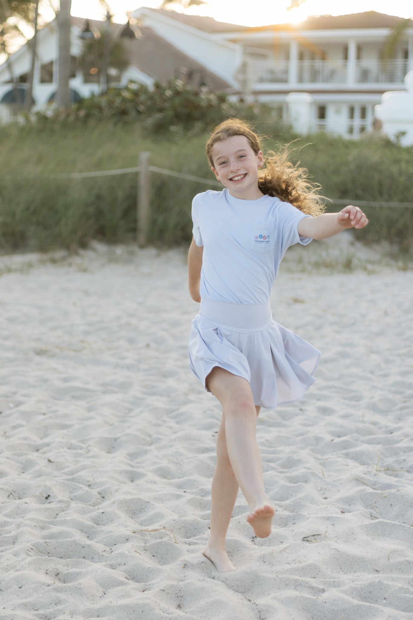 Young dancer twirling joyfully on a sandy beach at sunset with wind-swept hair and a light dress.