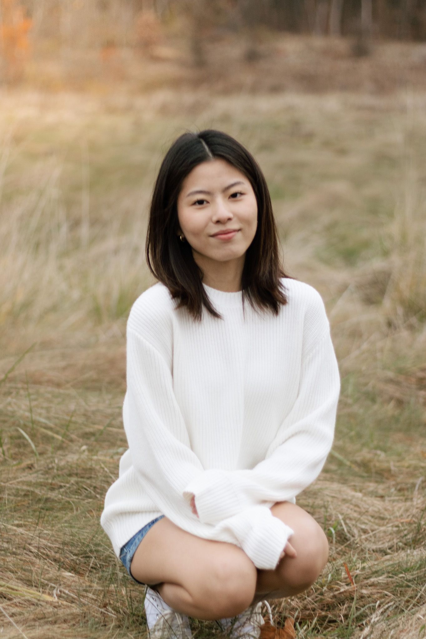 Casual outdoor portrait in white sweater against autumn field backdrop.