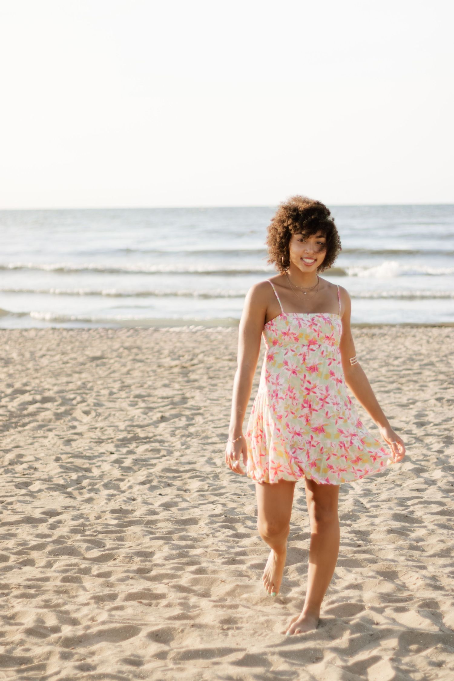 Playful sequence of a floral sundress on sandy beach with ocean waves in background.