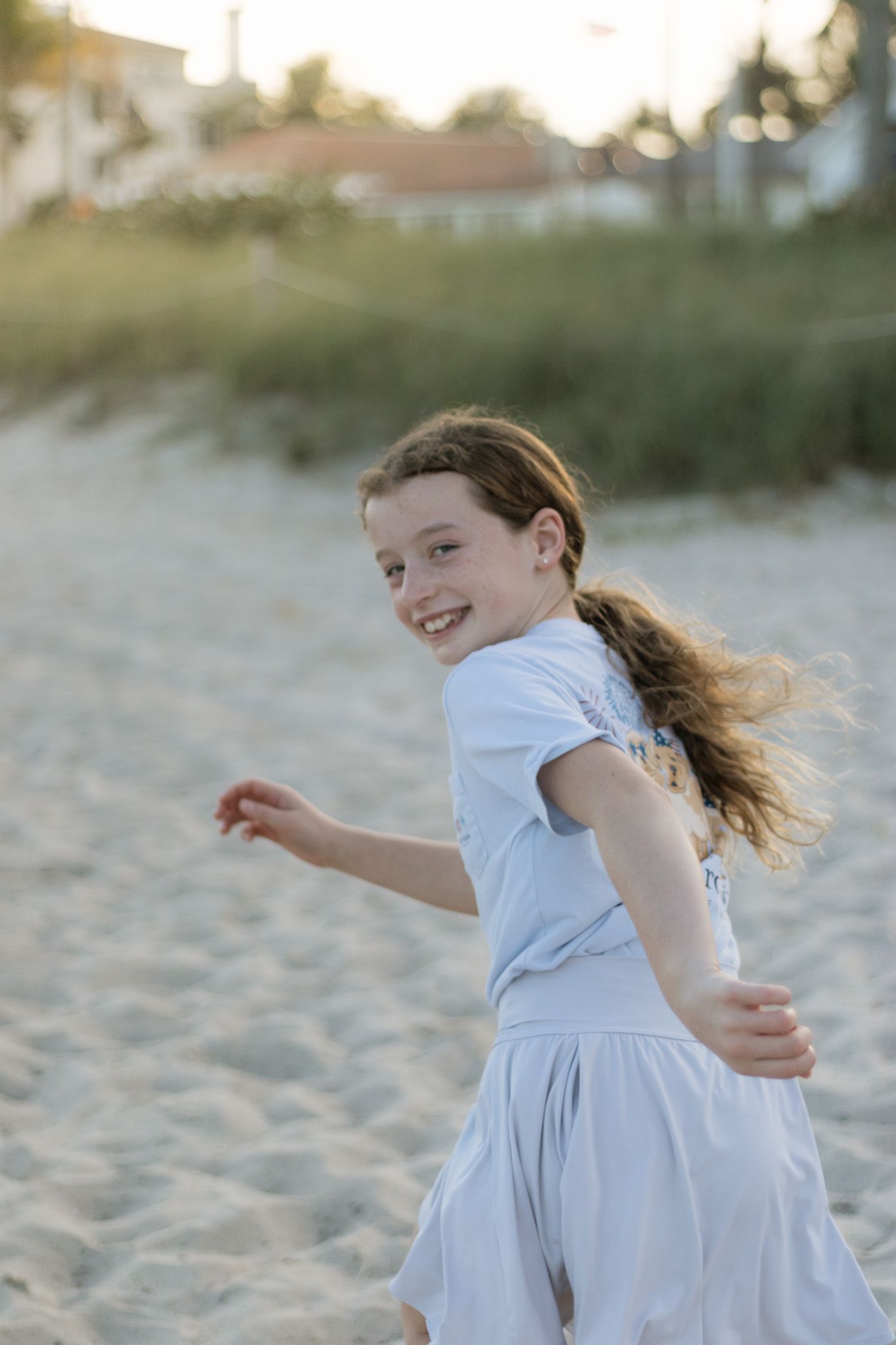 A joyful child twirling in a white dress on the beach at sunset during her family photos in Fort Lauderdale, FL