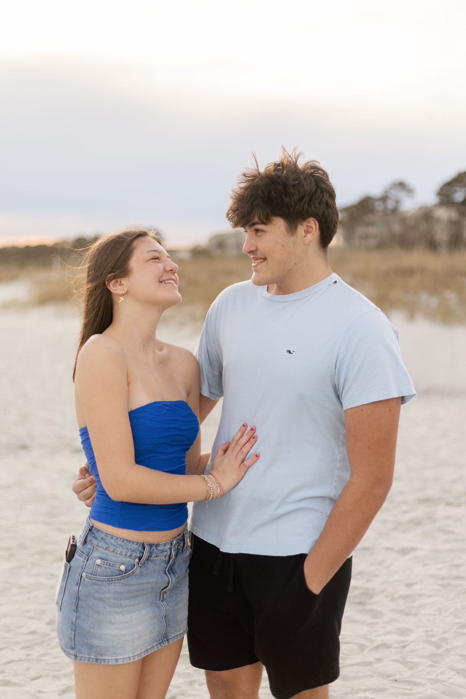 A couple shares romantic moments on a sandy beach while wearing casual summer outfits in a series of candid shots.