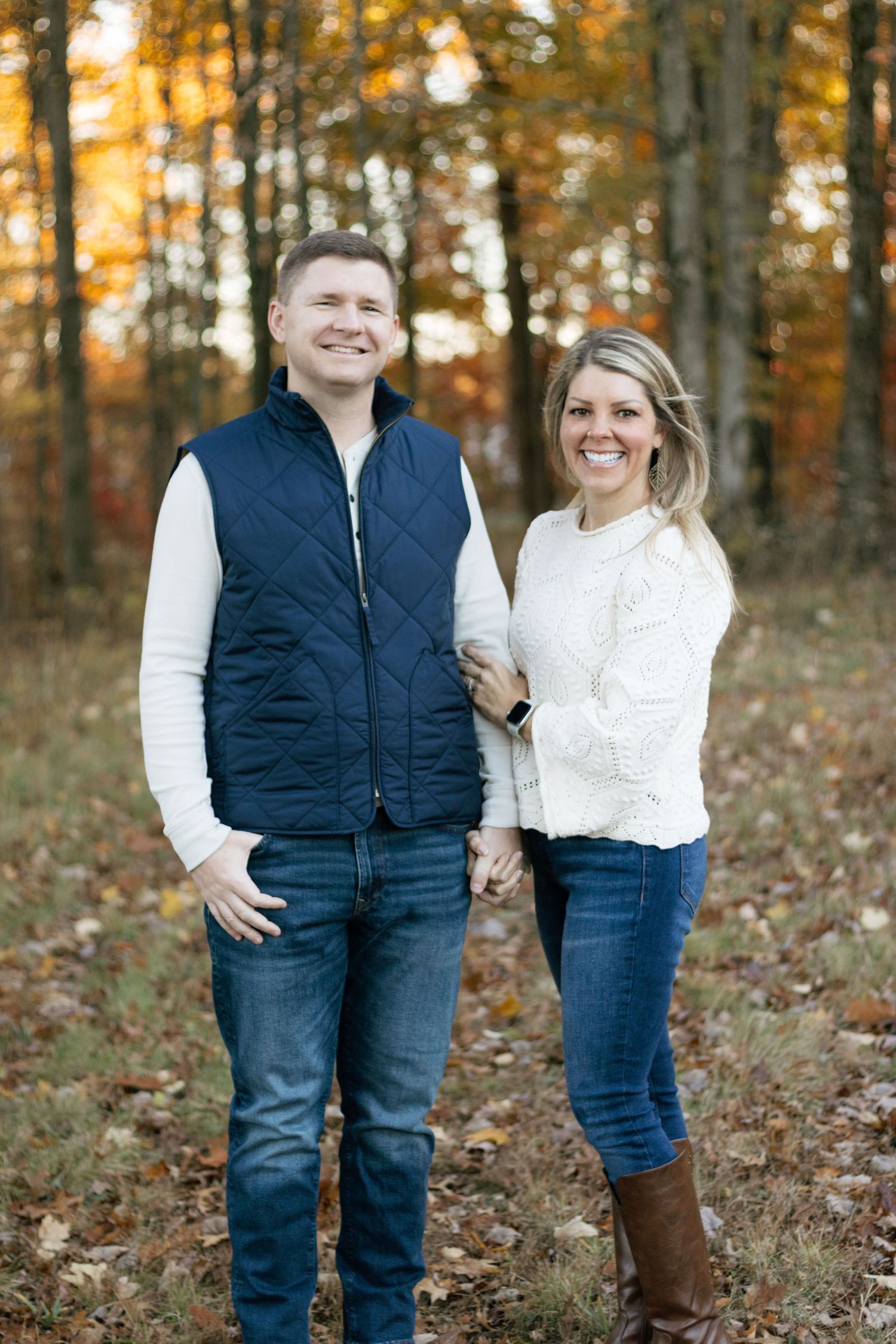 Couple in coordinated outfits poses playfully among fall foliage in wooded setting during their Hudson, OH couples photoshoot