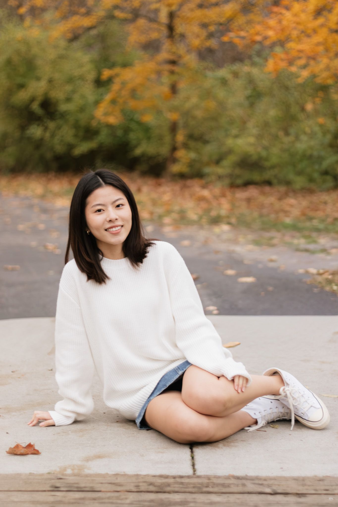 An autumn portrait on concrete on the bridge at Station Road Bridge Trailhead wearing white sweater and denim shorts.