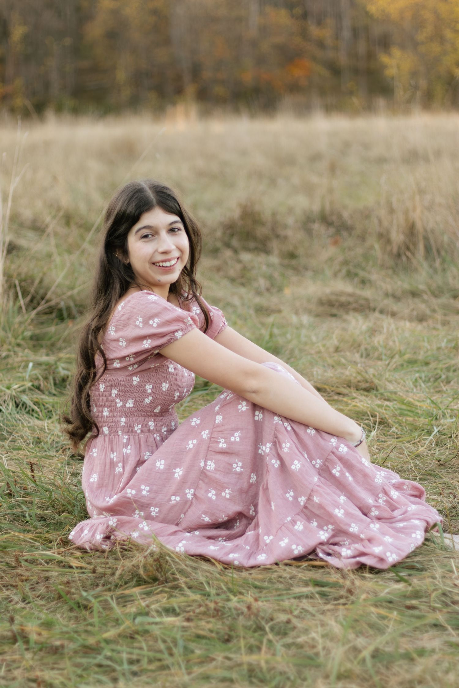 Portrait series in pink floral dress sitting in autumn field during golden hour.