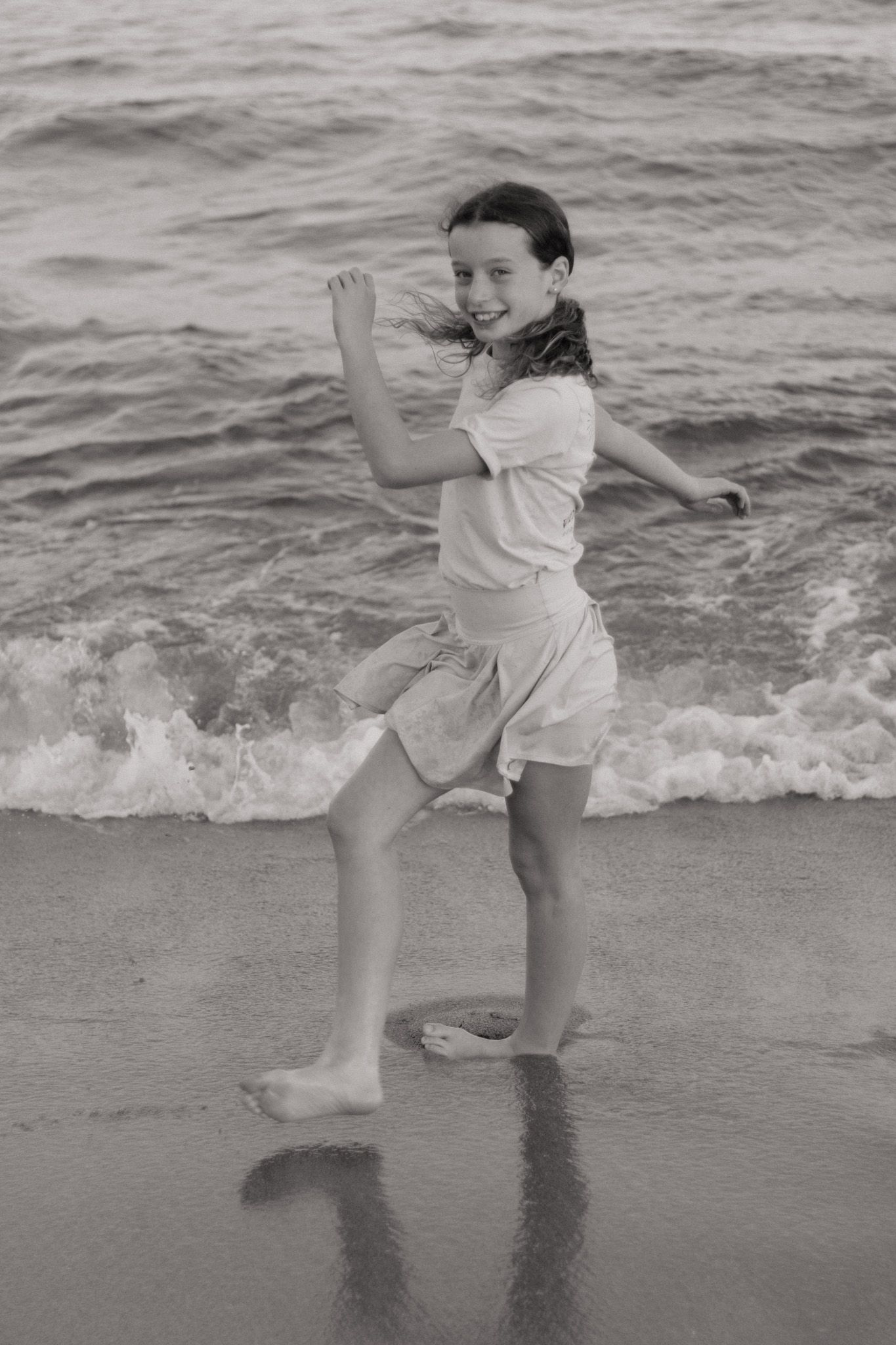 Black and white photo of a child playing in the ocean waves at the beach.