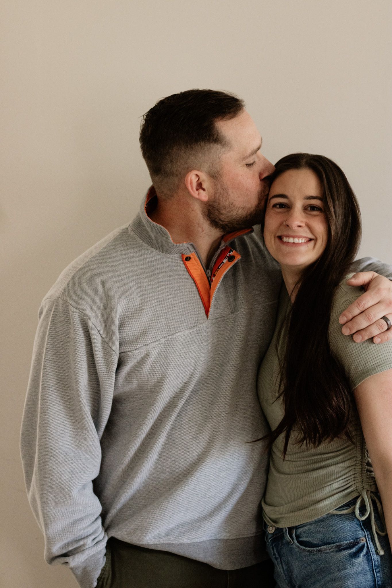 Romantic couple shares tender moments in casual clothing against neutral background in their Akron Ohio home during a family photshoot