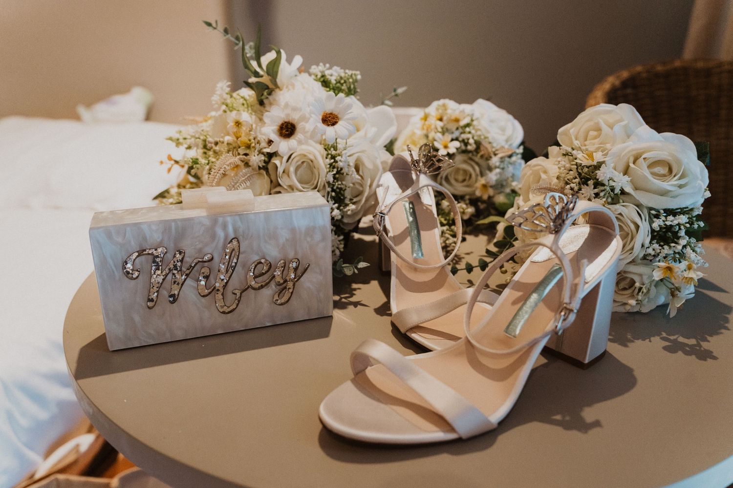Wedding details featuring elegant white high heel sandals and floral arrangements with a decorative sign.