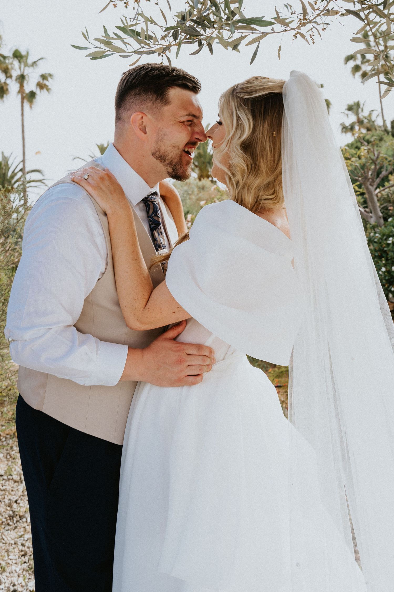 Romantic wedding portrait of couple embracing under palm trees in natural light.