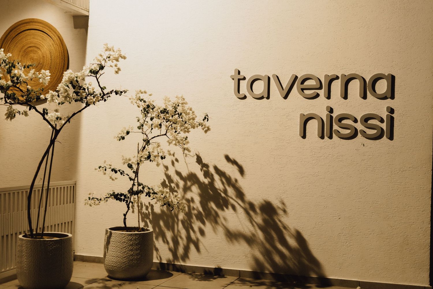 Restaurant signage reading 'taverna nissi' on a neutral wall with decorative plant shadows.