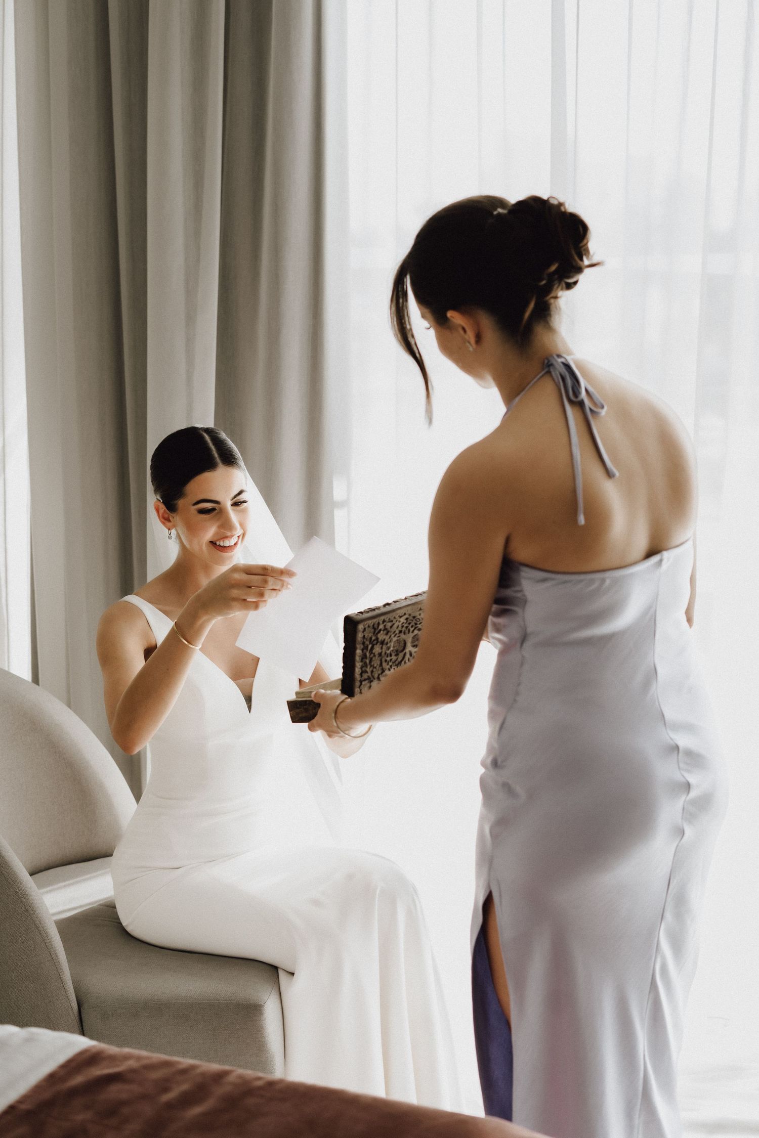 Two women share a moment while reading cards during wedding preparations.