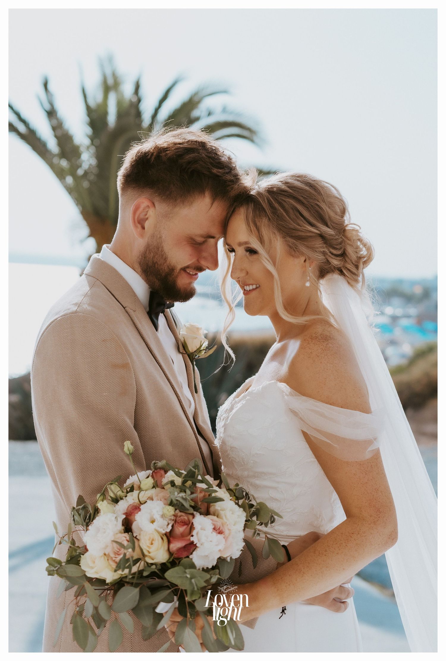 Intimate wedding moment captured with palm trees and ocean backdrop as couple shares tender embrace.