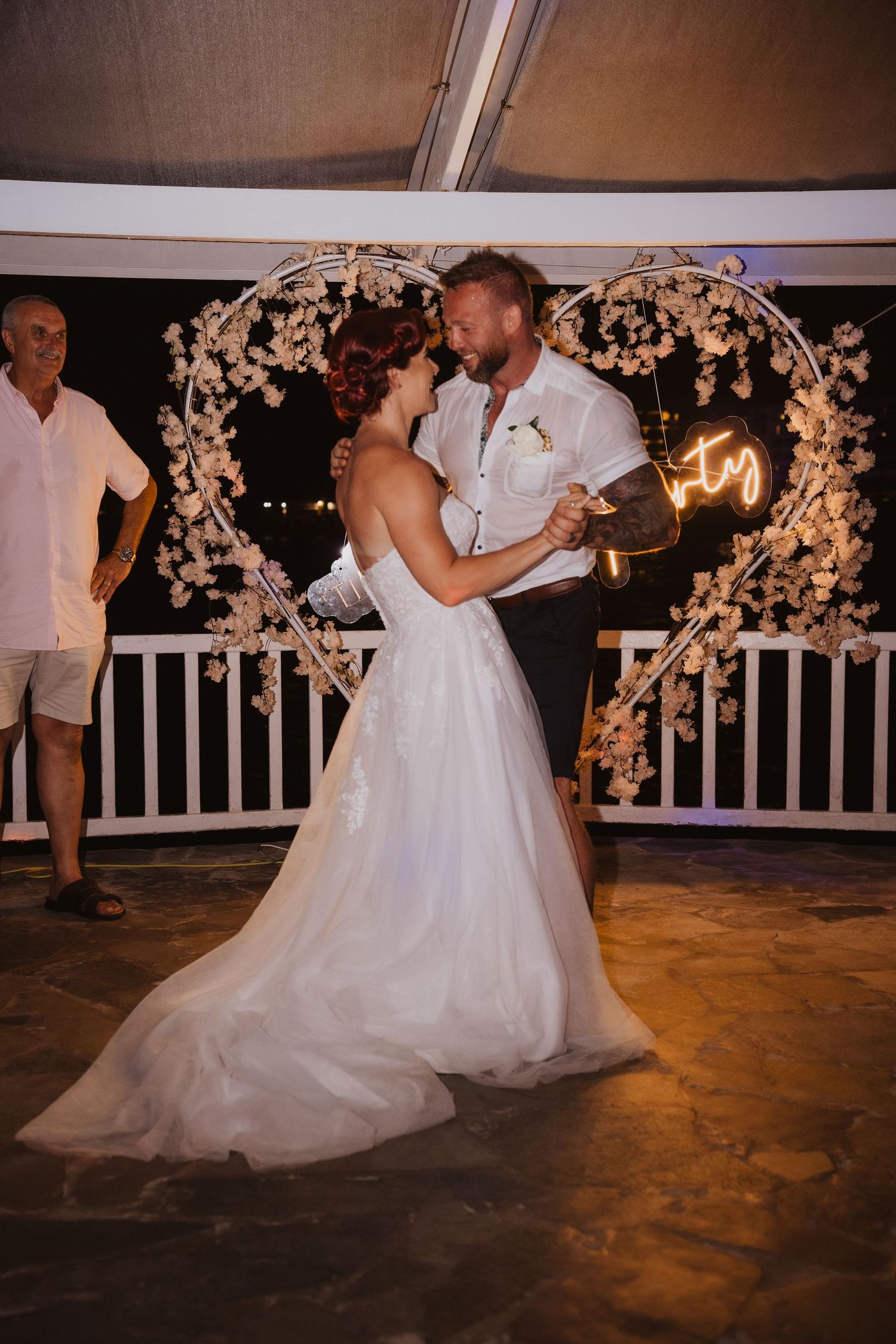 Wedding dance moment under a beautifully lit floral arch at night.