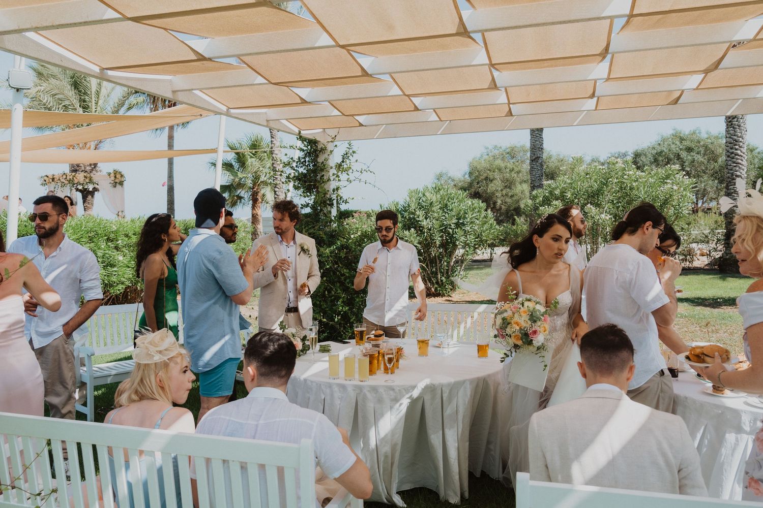 Casual outdoor wedding reception with guests dining under cream-colored canopy.