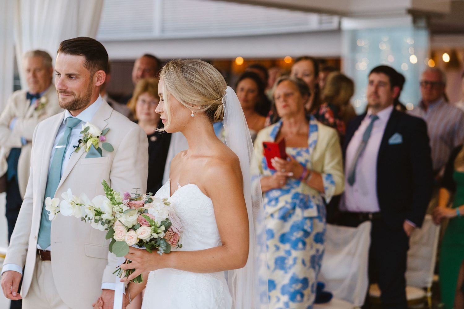 Wedding couple standing at altar during ceremony with guests watching in summer attire.