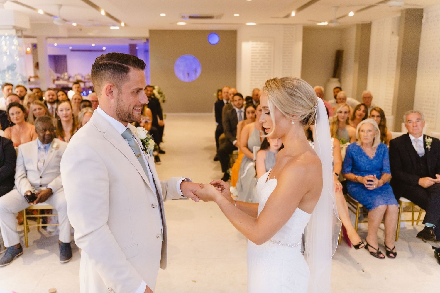 A joyful moment during the ring exchange at an indoor wedding ceremony.