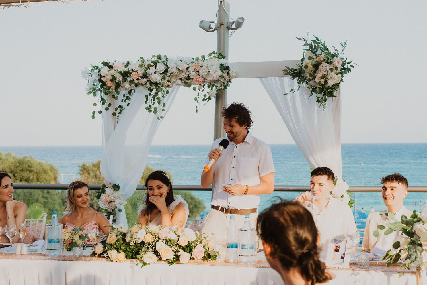 Wedding toasts and speeches during outdoor reception with ocean backdrop.