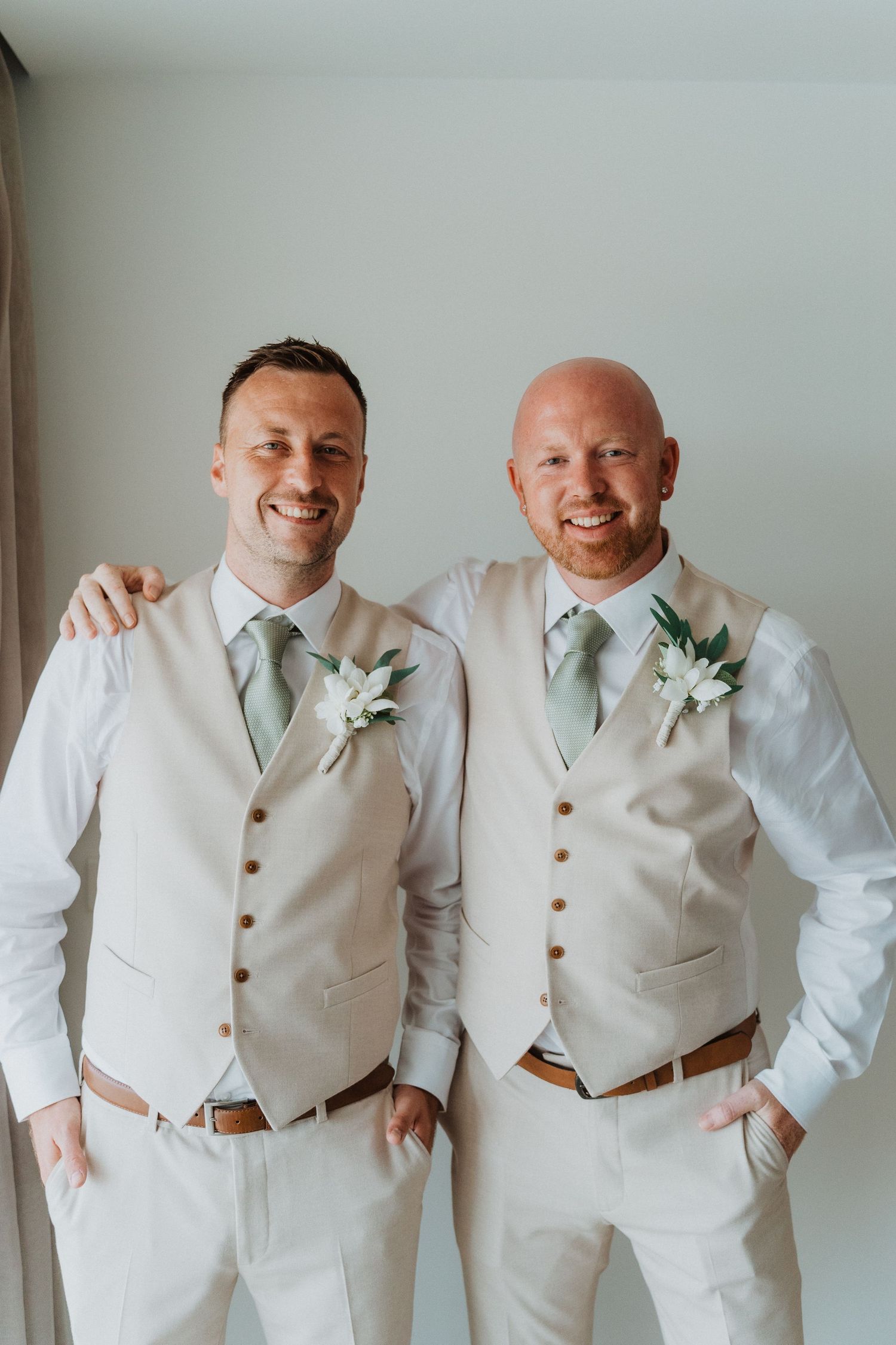 Two people wearing matching cream vests, mint green ties and white boutonnières pose together at a formal event.