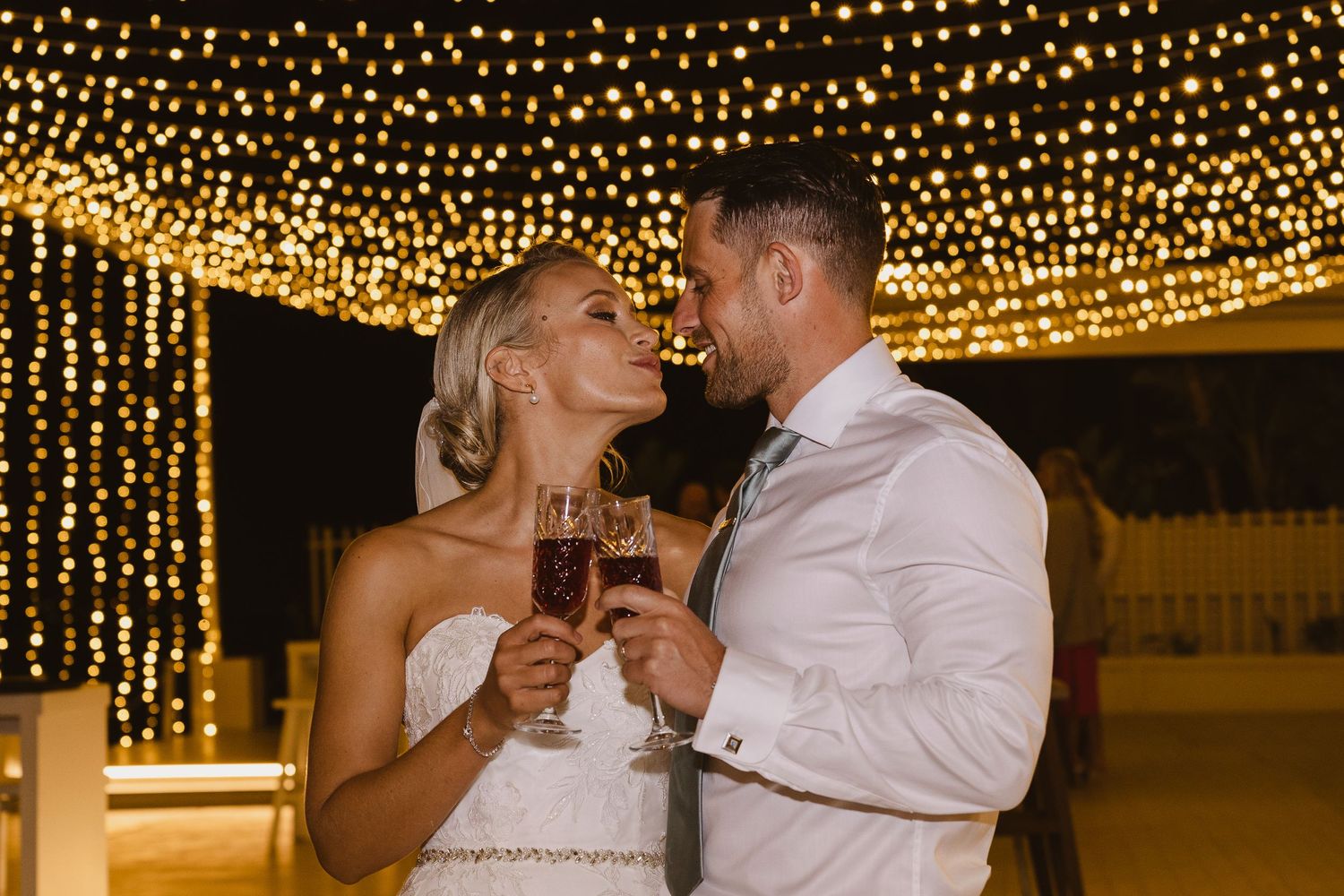 Couple shares a tender moment during their wedding toast beneath sparkling overhead lights.