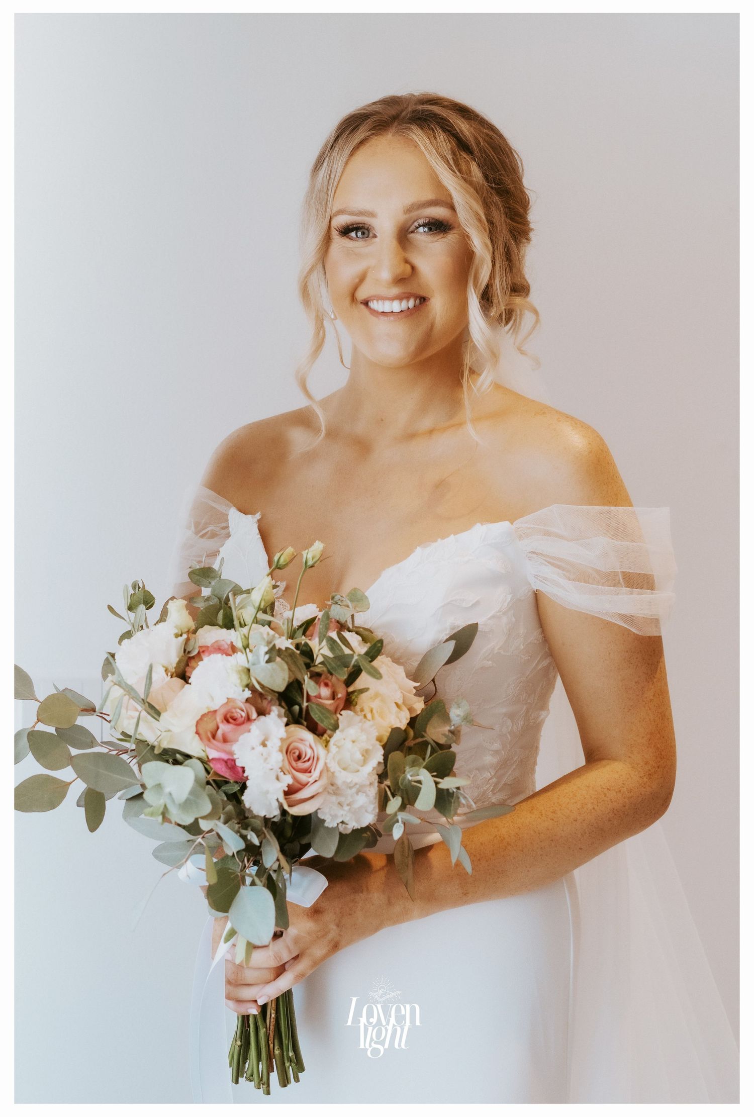 Bride in off-shoulder white gown holding romantic blush and white bouquet.