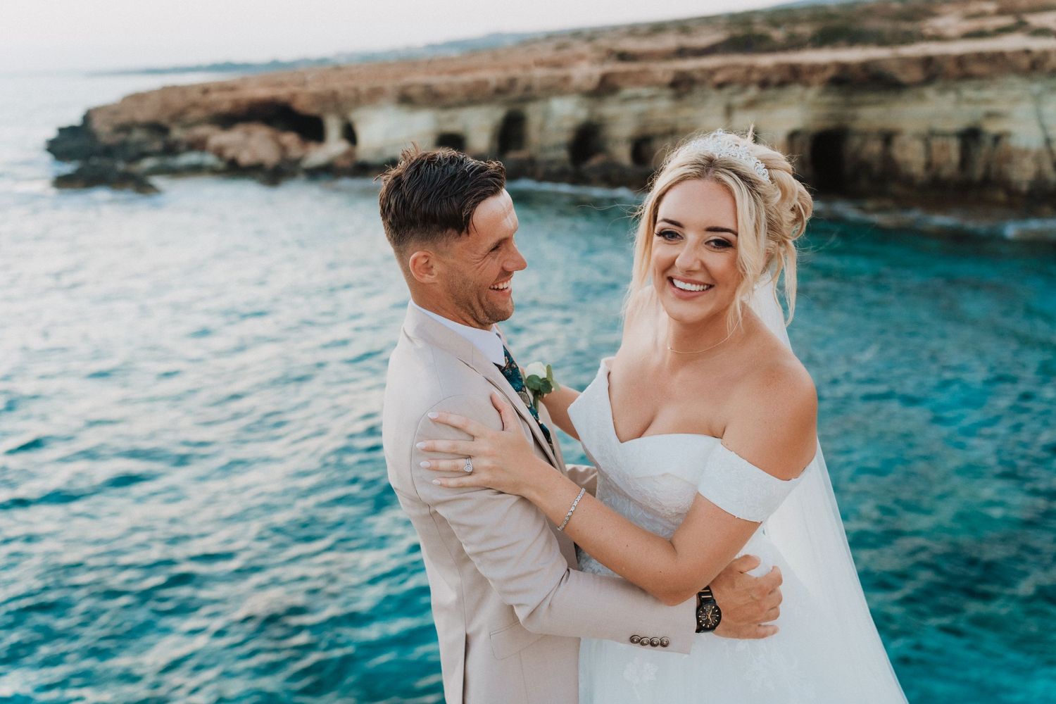 Beachside wedding portrait with crystal blue waters and coastal cliffs in the background.