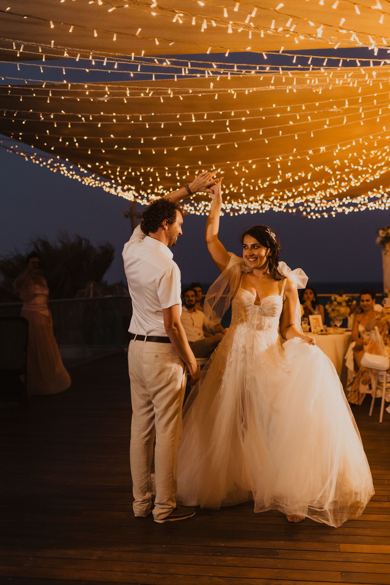 Newlyweds share their first dance under a romantic canopy of twinkling lights at an outdoor evening reception.