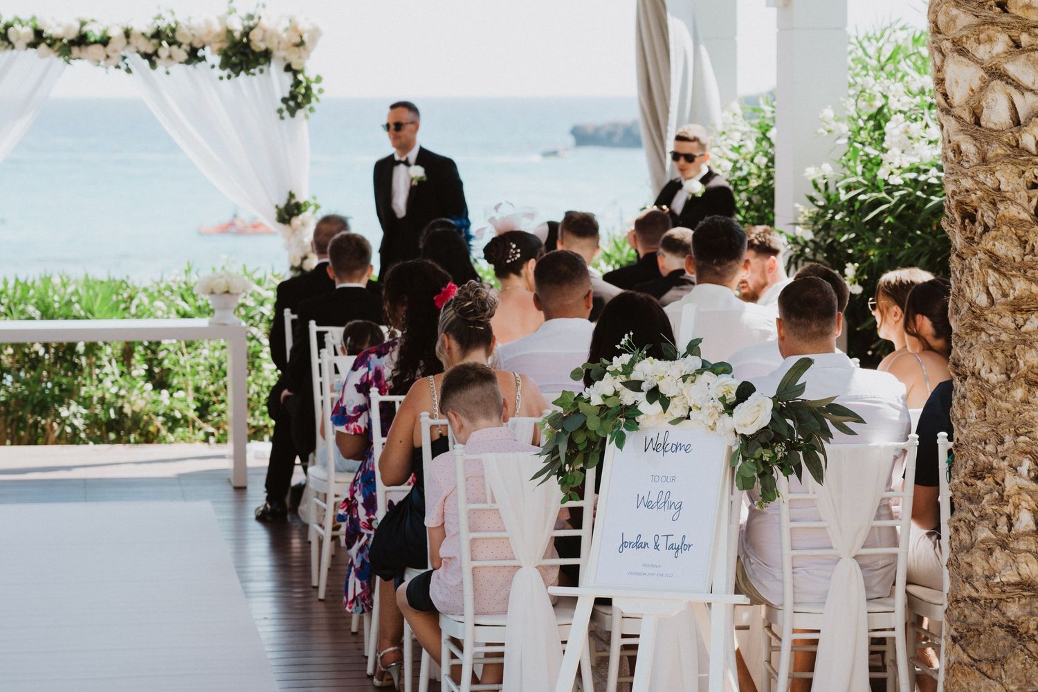 Wedding ceremony in progress under a white pergola with floral arrangements.