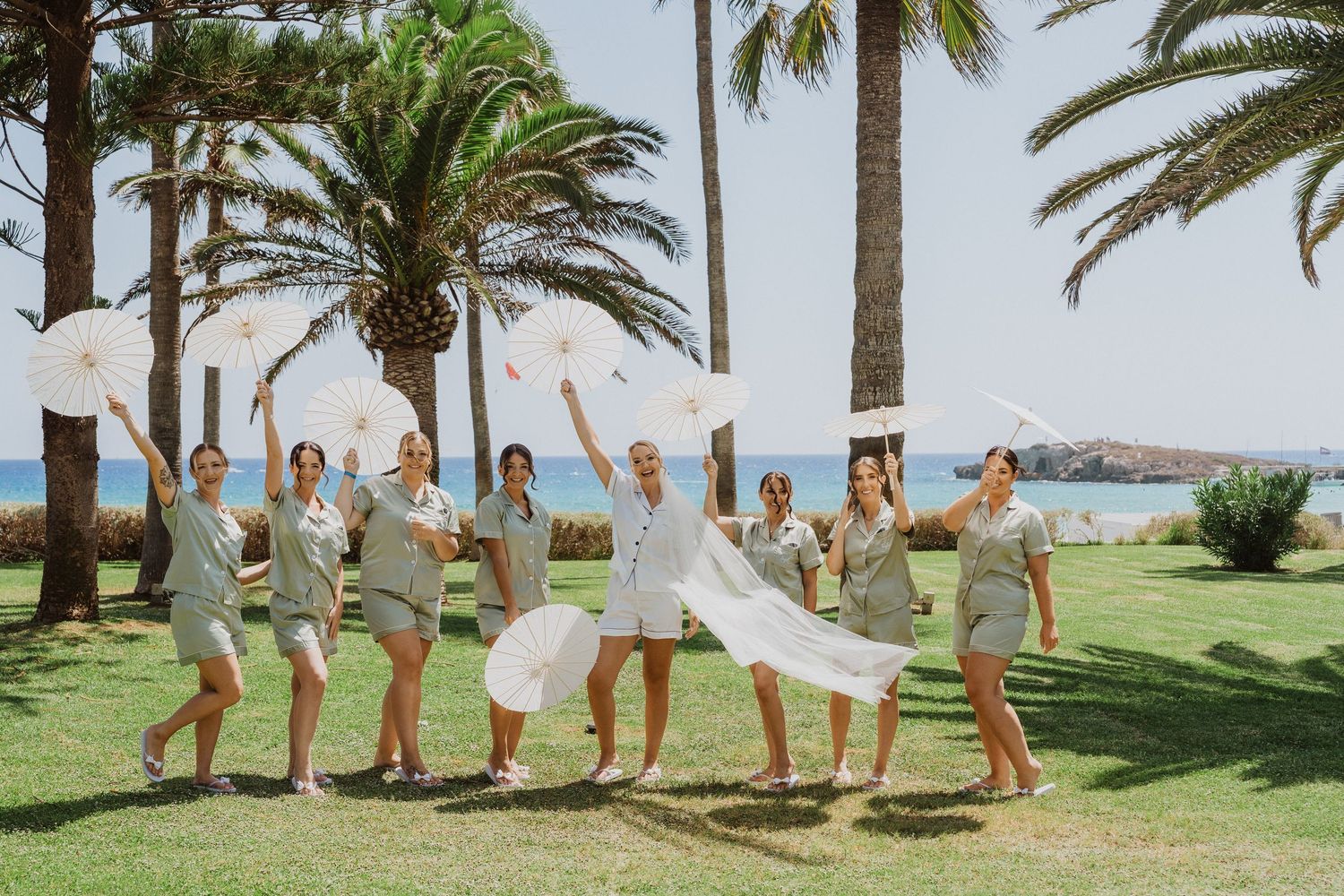 Wedding party members jumping and posing energetically on a palm tree-lined lawn.