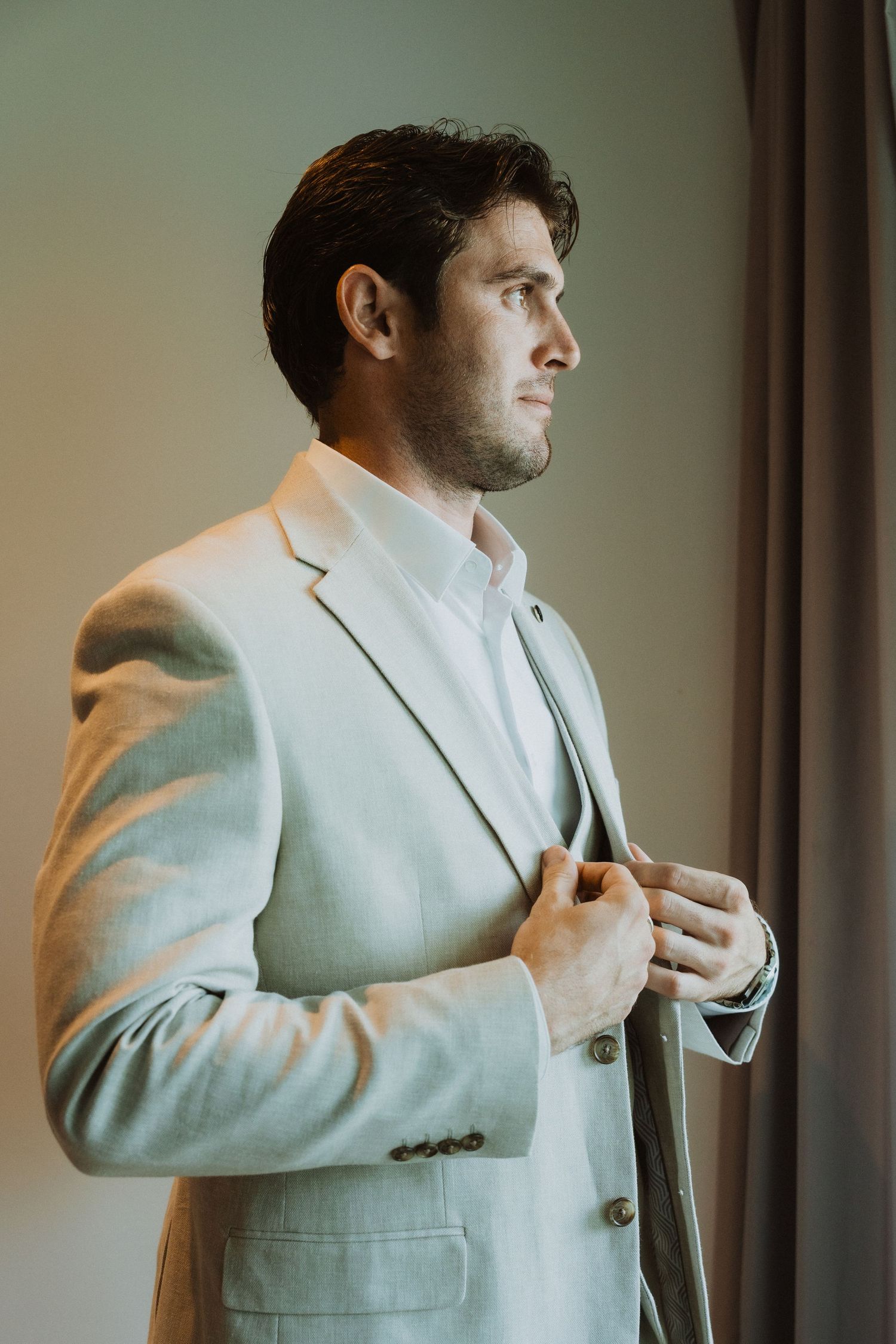 Side profile of a person wearing a light colored suit and white shirt in natural window light.