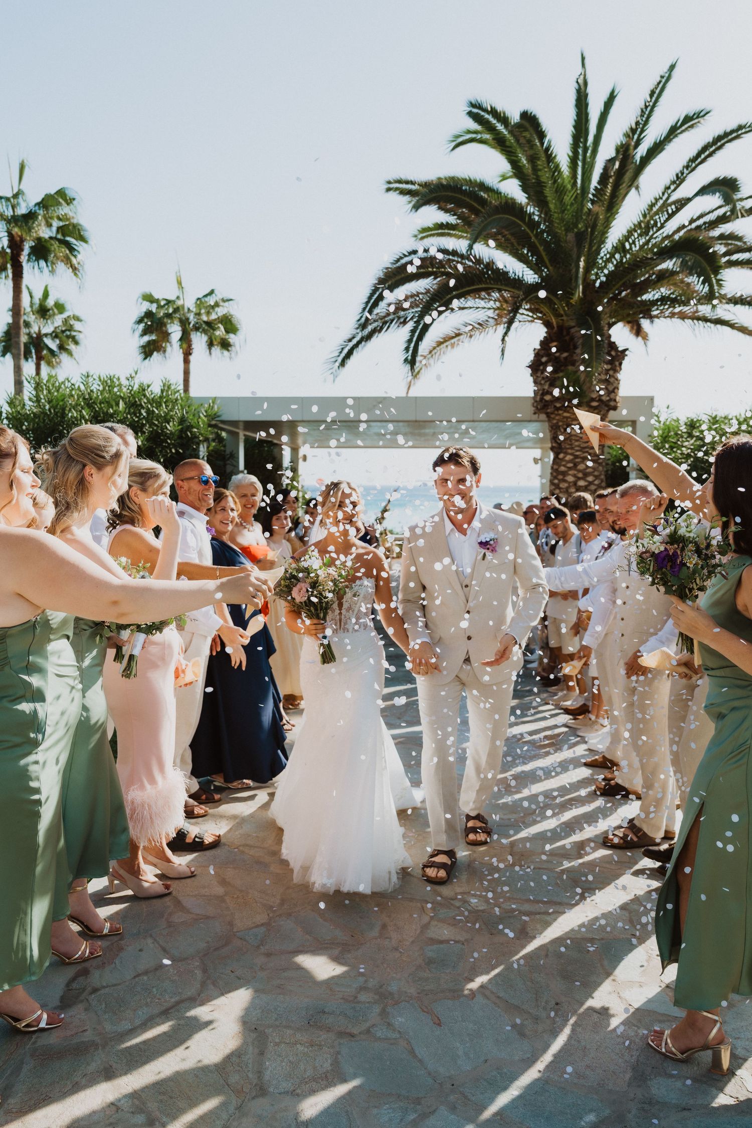Celebratory confetti shower during a beachside wedding ceremony with palm trees and natural lighting.