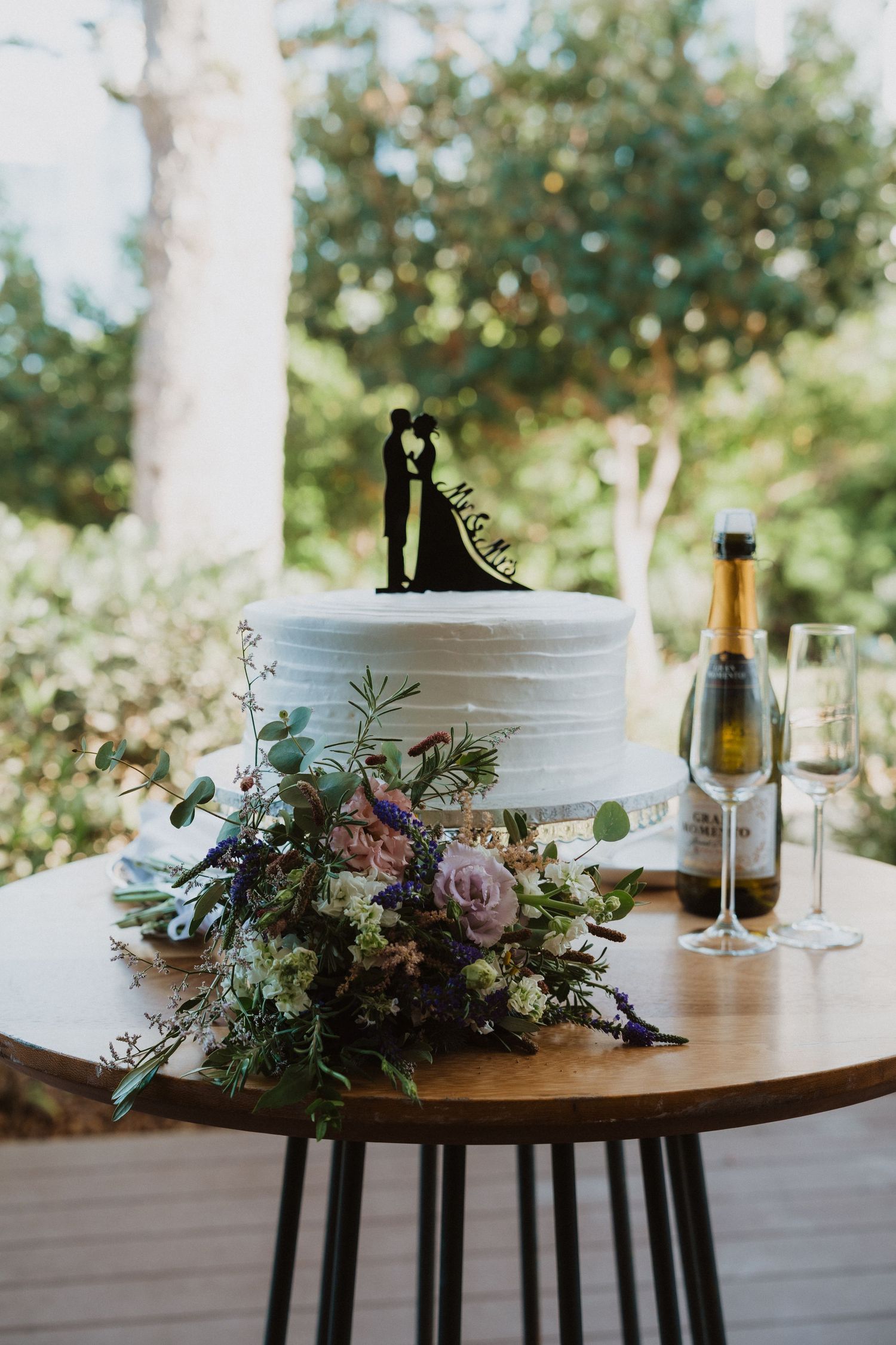 Elegant white wedding cake decorated with pink and purple flowers on wooden table.