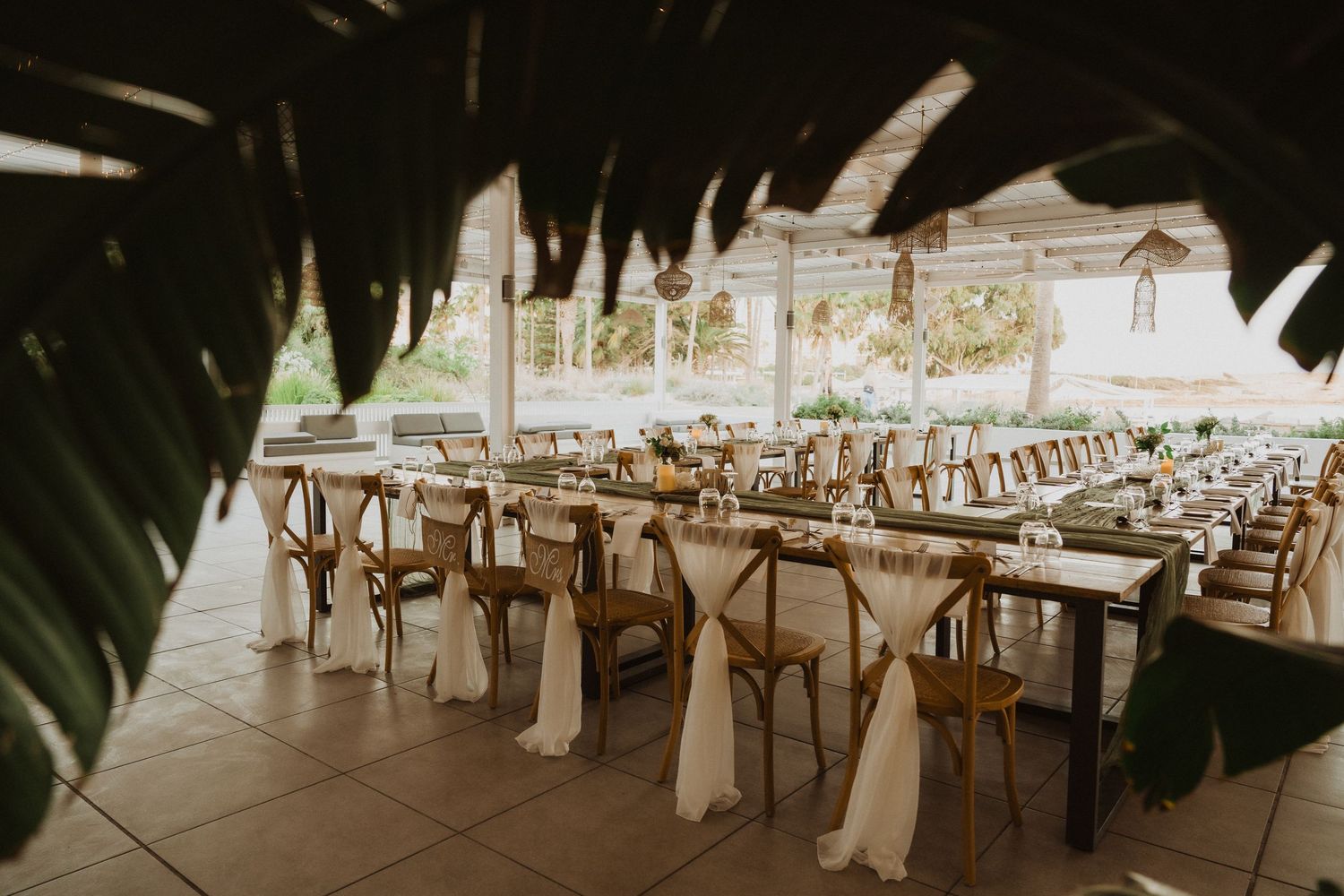 Long banquet tables set for an elegant outdoor wedding reception with white fabric chair decor.