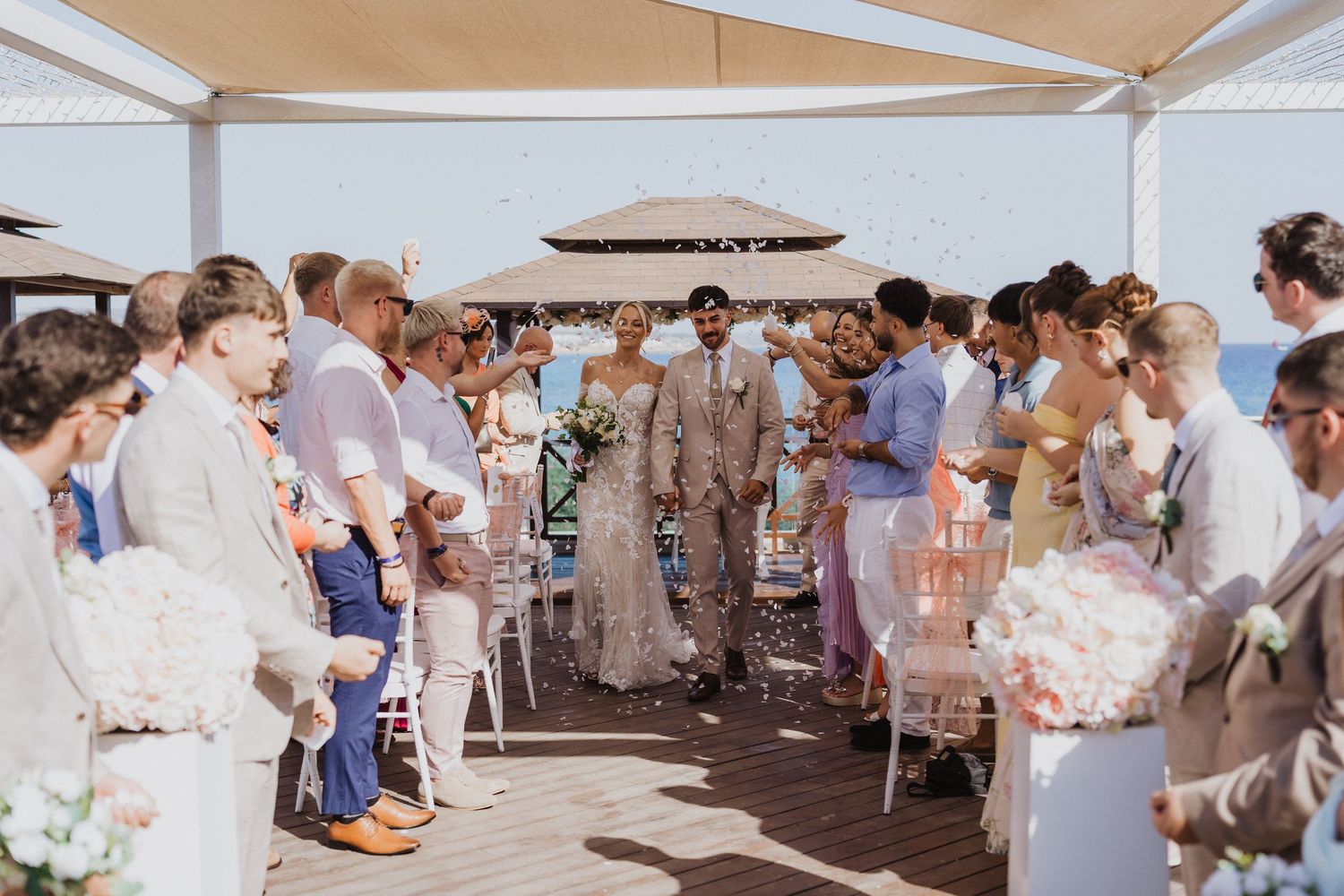 Joyful wedding celebration with guests throwing confetti under a covered outdoor venue.