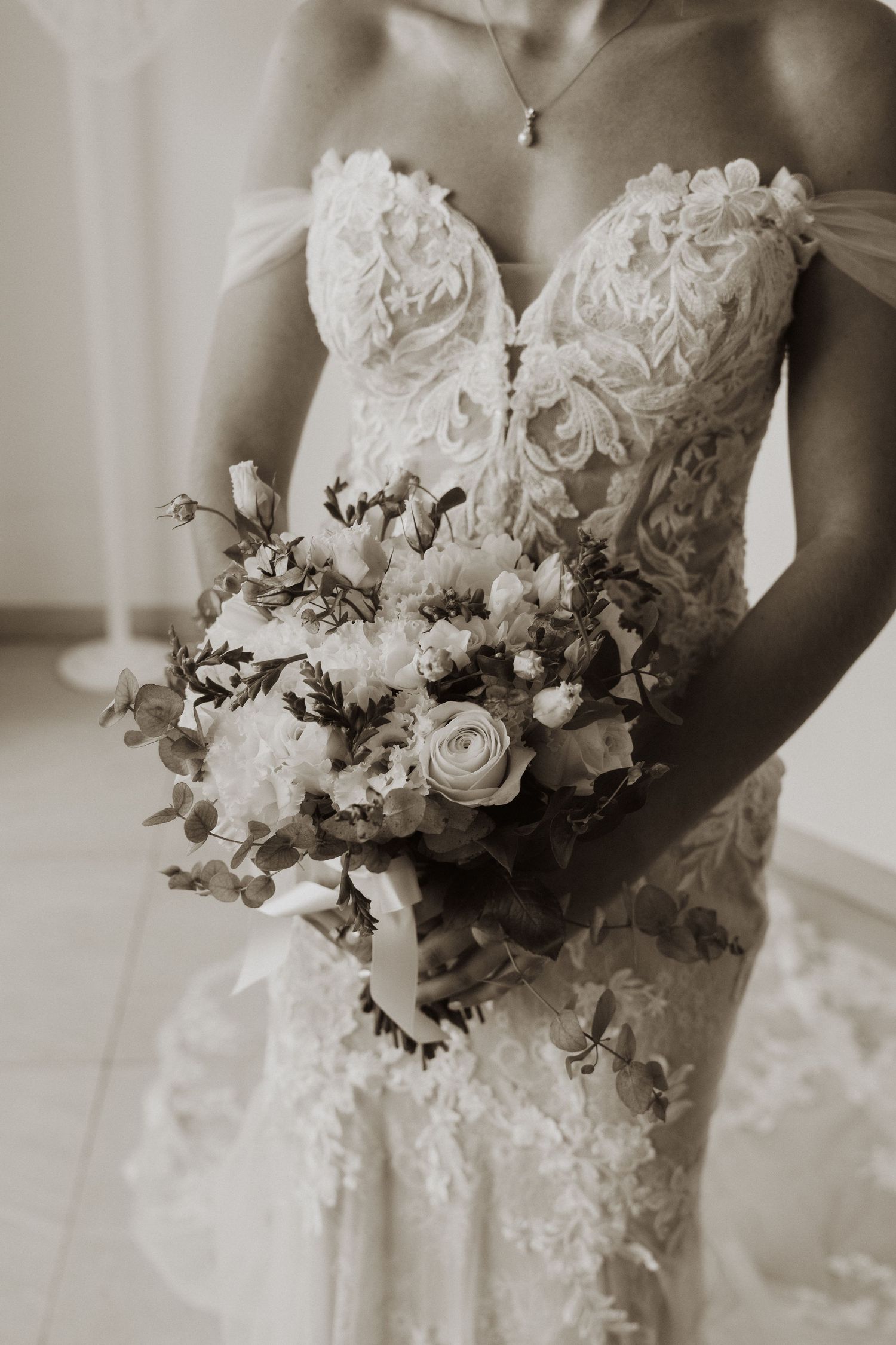 Black and white detail shots of a bridal bouquet with white roses against a lace wedding dress.