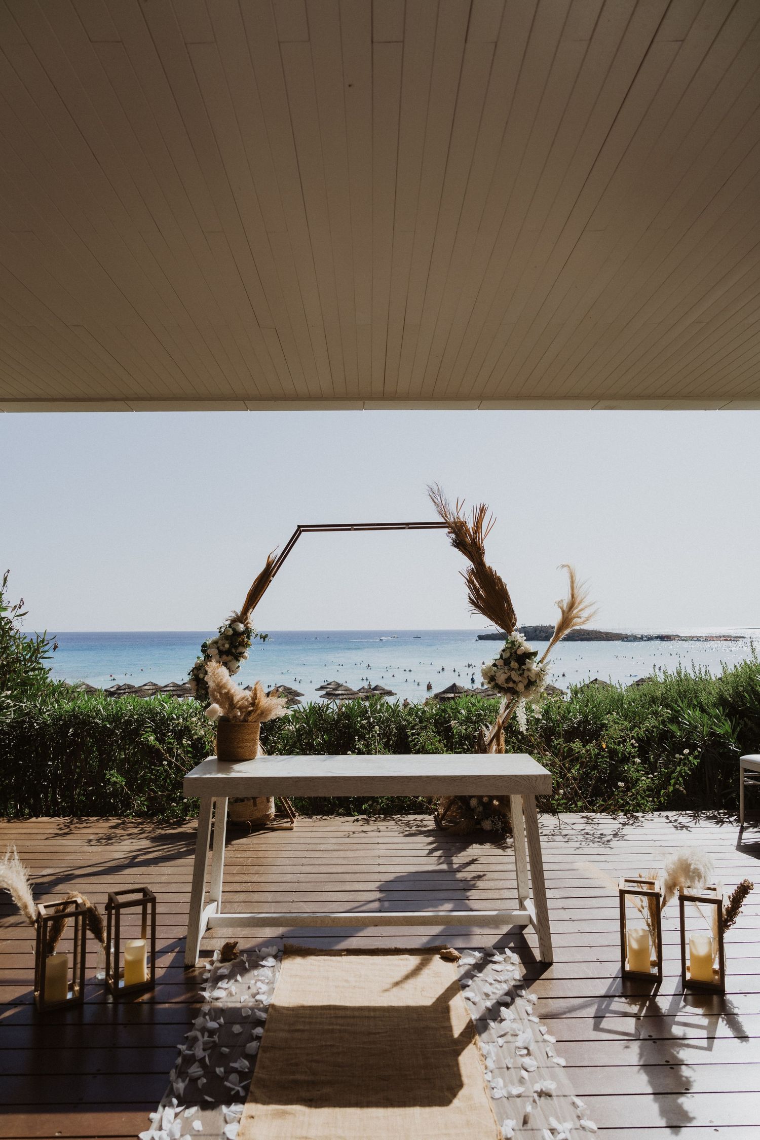 Boho wedding arch with dried flowers set against ocean backdrop on wooden deck.